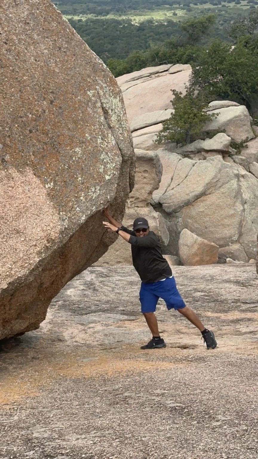 A hiker playfully pretending to push a huge pink granite boulder at Enchanted Rock