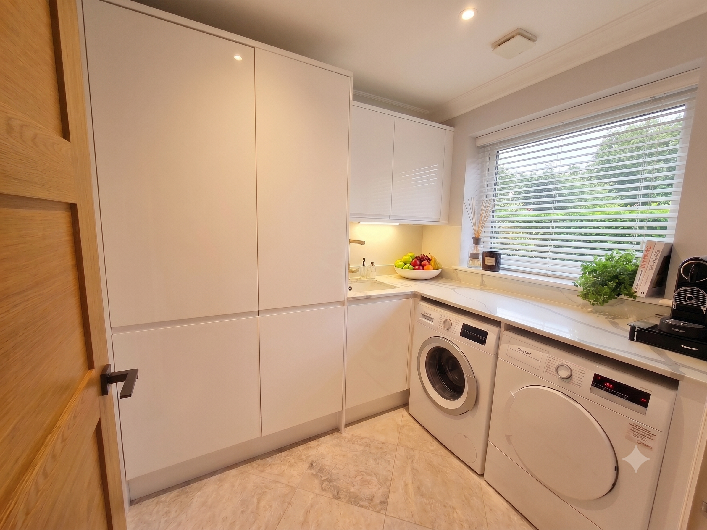 Kitchen with white cabinets, a window with blinds, a bowl of fruit, and a washing machine.