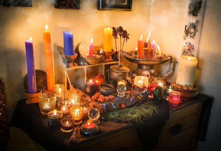A dimly lit table decorated with colorful candles, glass jars, and small objects, creating a cozy, mystical atmosphere.
