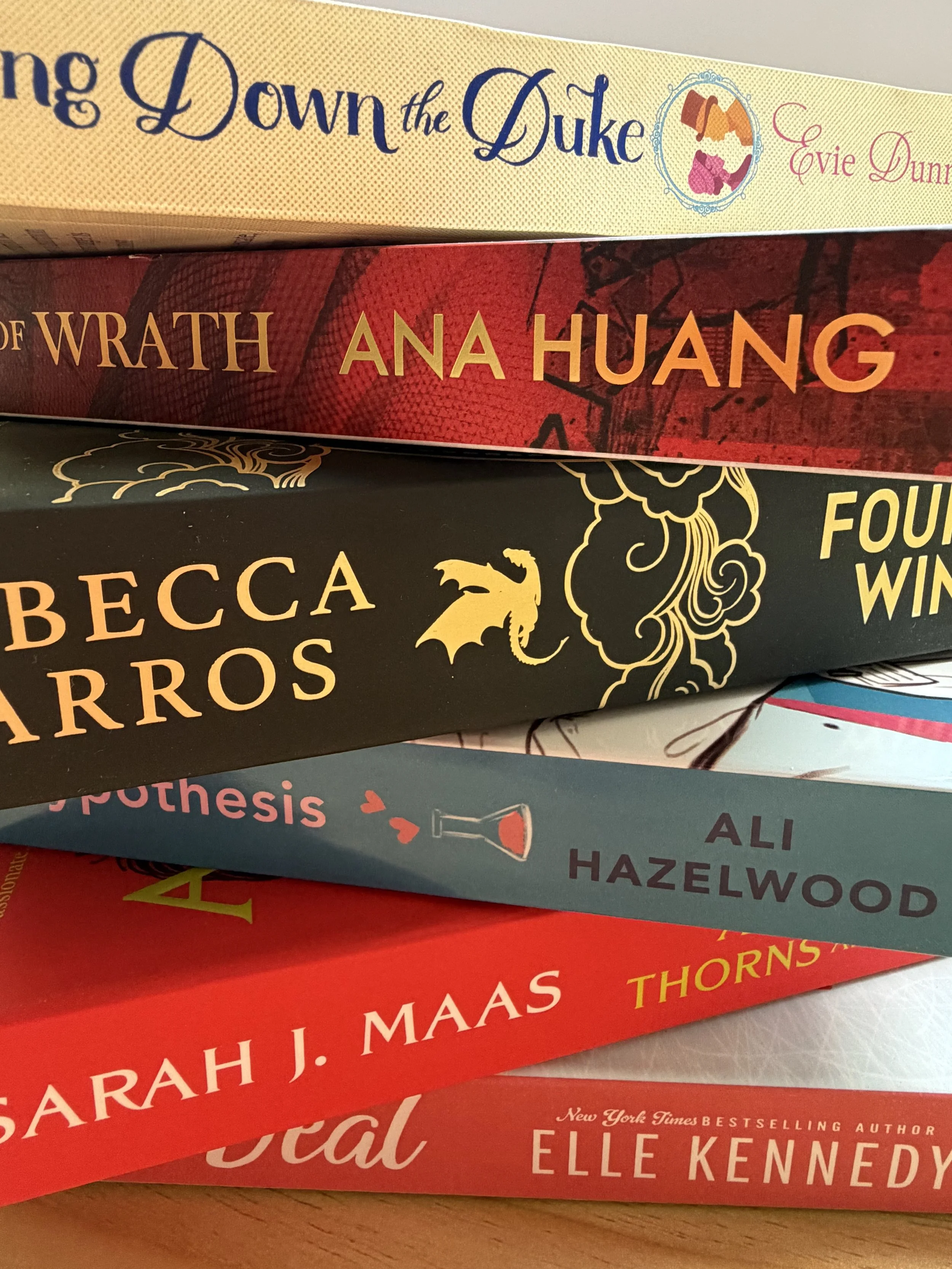 Stack of five books with colorful covers, titles, and authors visible, including 'Down the Duke' by Evie Dunmore, 'Wrath' by Ana Huang, 'Becca' by Sarah J. Maas, and 'Evil' by Elle Kennedy.