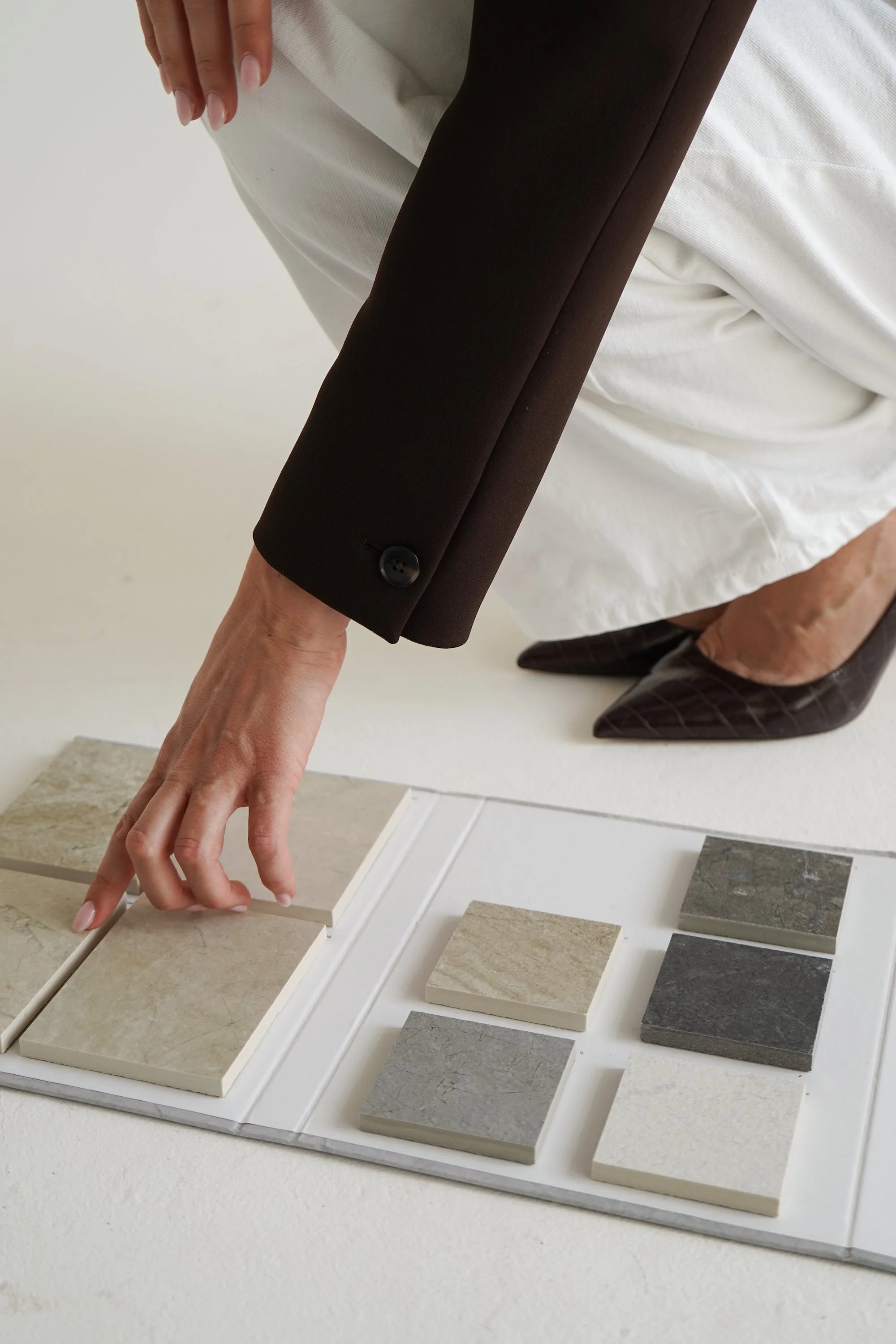 Person's hand reaching out to touch a tile sample on a display board with various beige and gray tile options.