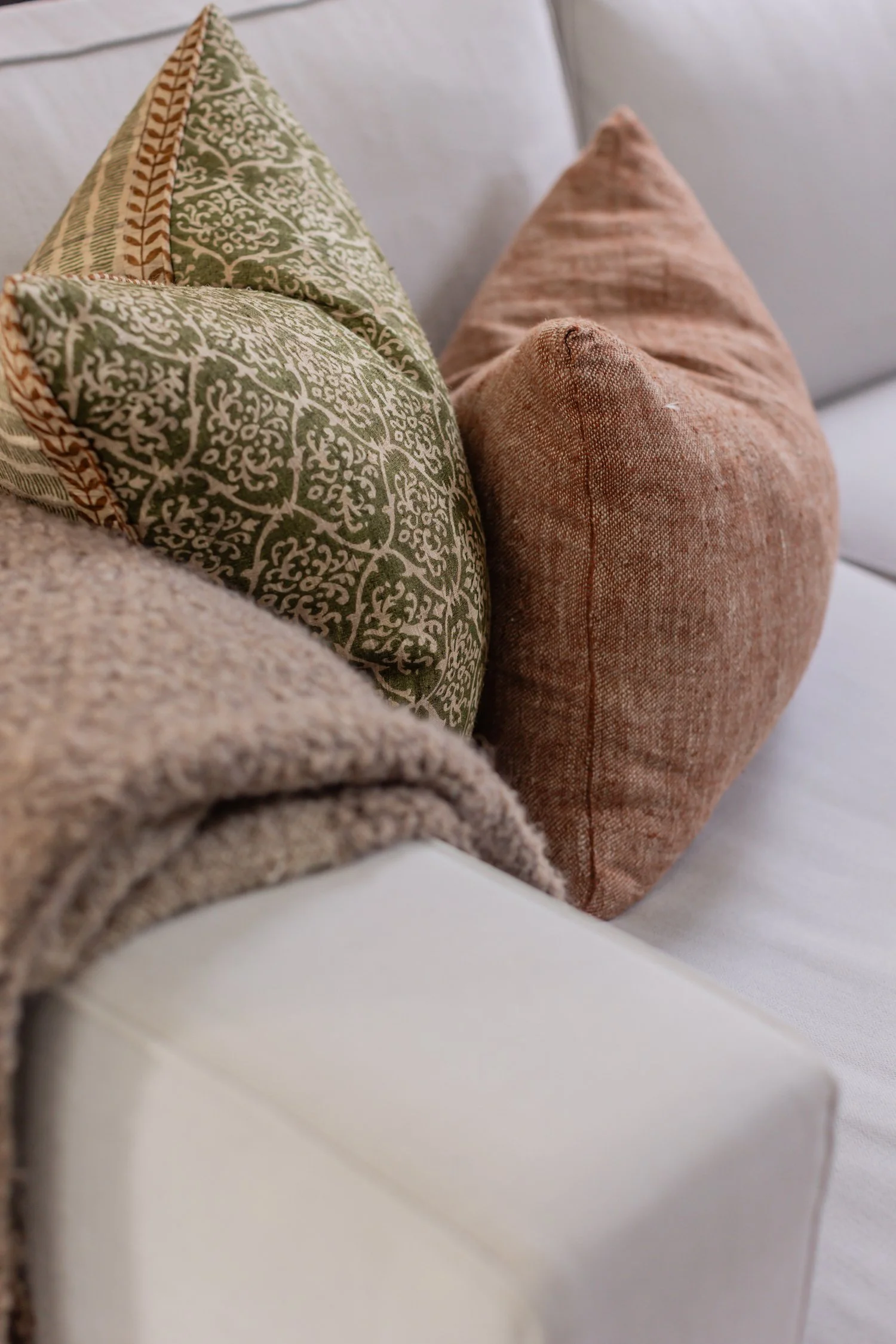 Close-up photo of two decorative pillows on a couch, one with green and tan intricate pattern and the other in solid brownish-orange fabric.
