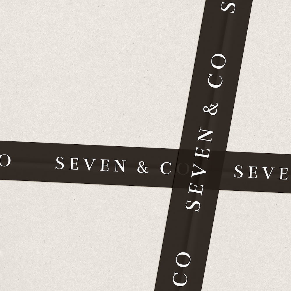 A beige surface with black strips of tape crossing each other, with the words "SEVEN & C O" printed on them.