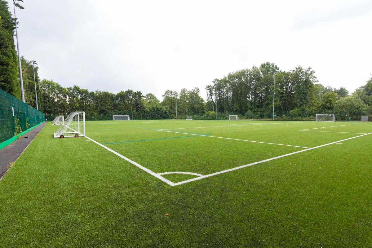An empty soccer field with artificial turf, multiple goals, and surrounded by trees.