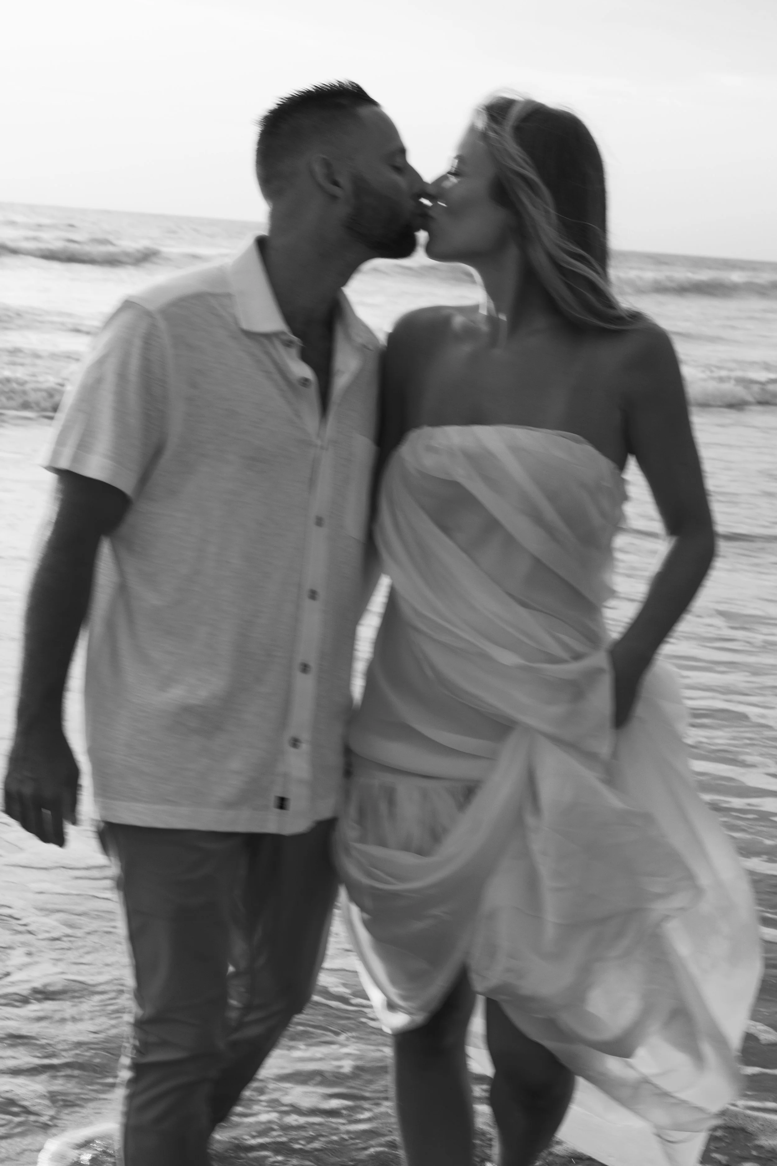 A man and woman are sharing a kiss on the beach with the ocean in the background.
