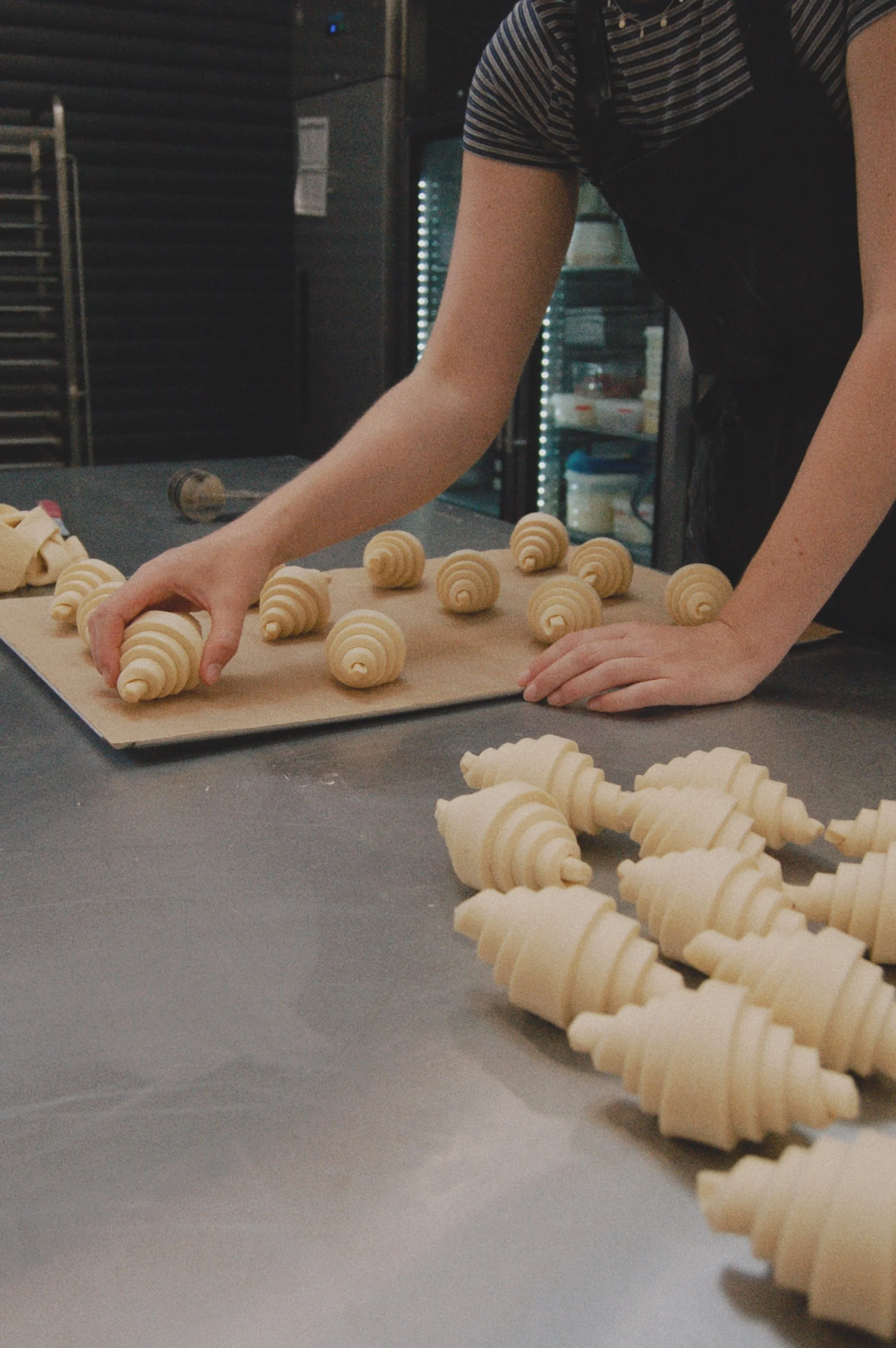 Person arranging uncooked croissant-shaped pastries on a baking sheet in a commercial kitchen.