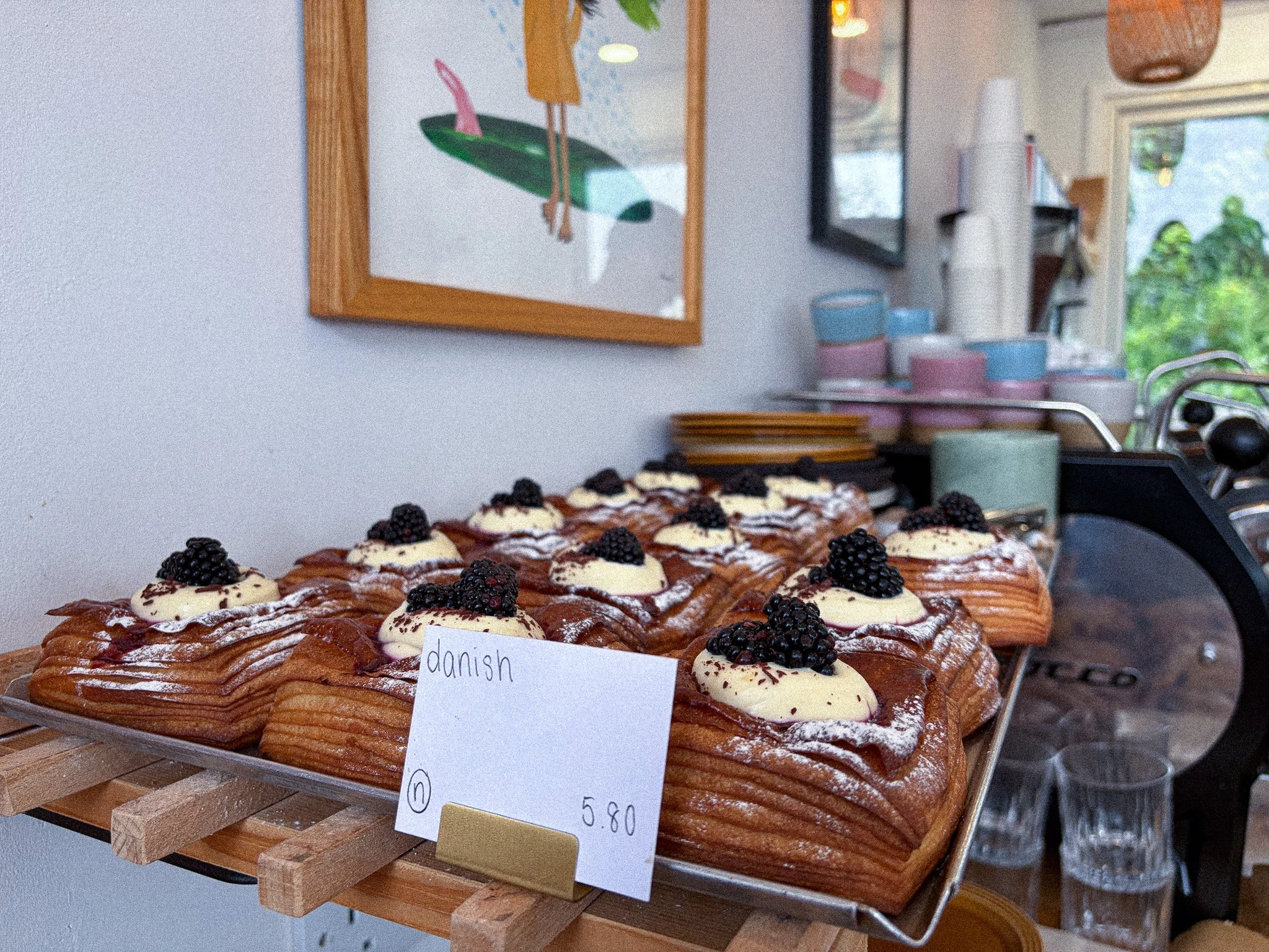 Danish pastry topped with cream and blackberries on a display tray with a handwritten price tag.