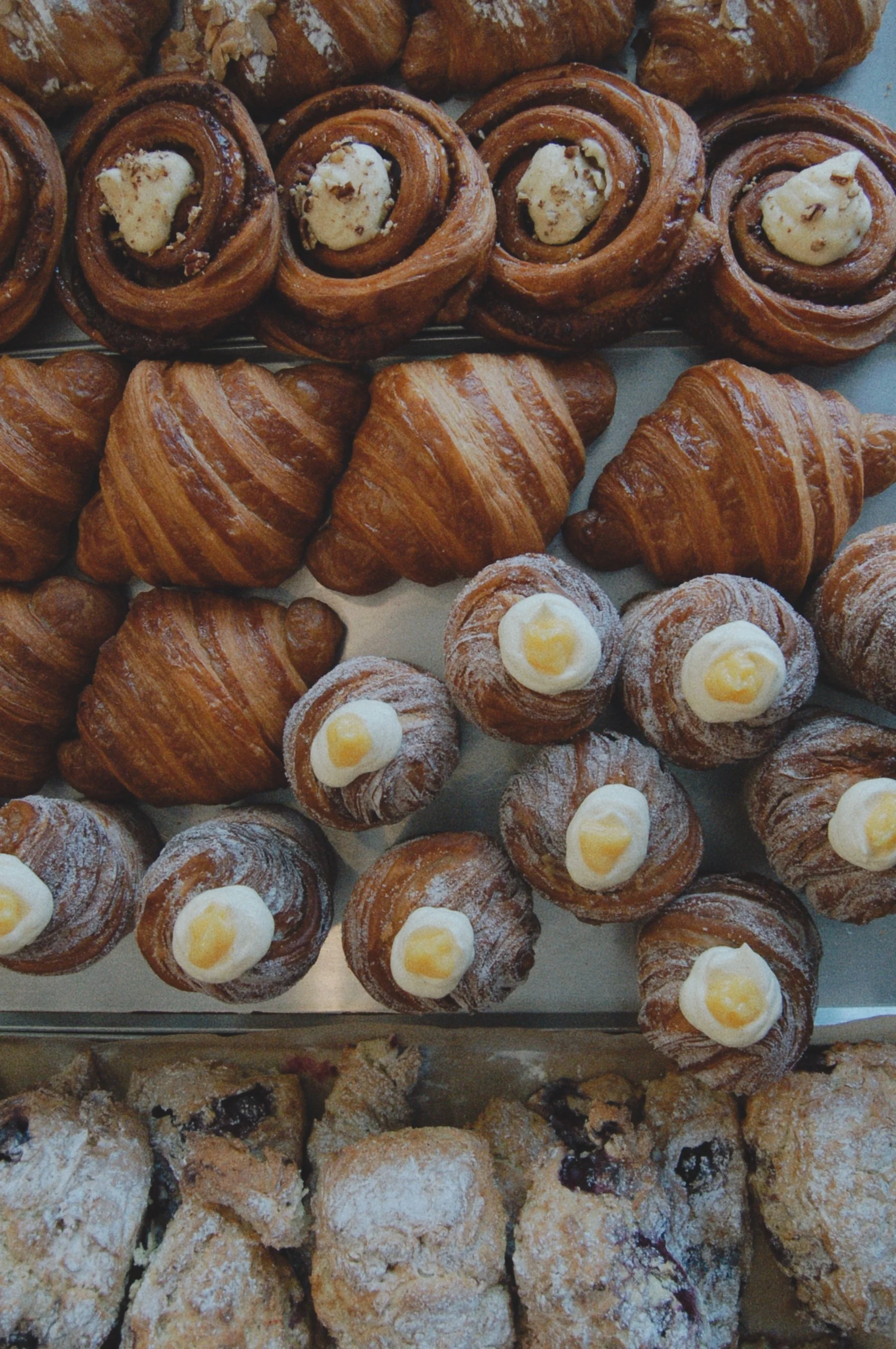 A variety of baked goods including croissants, cinnamon rolls with icing, and other pastries at a bakery display.