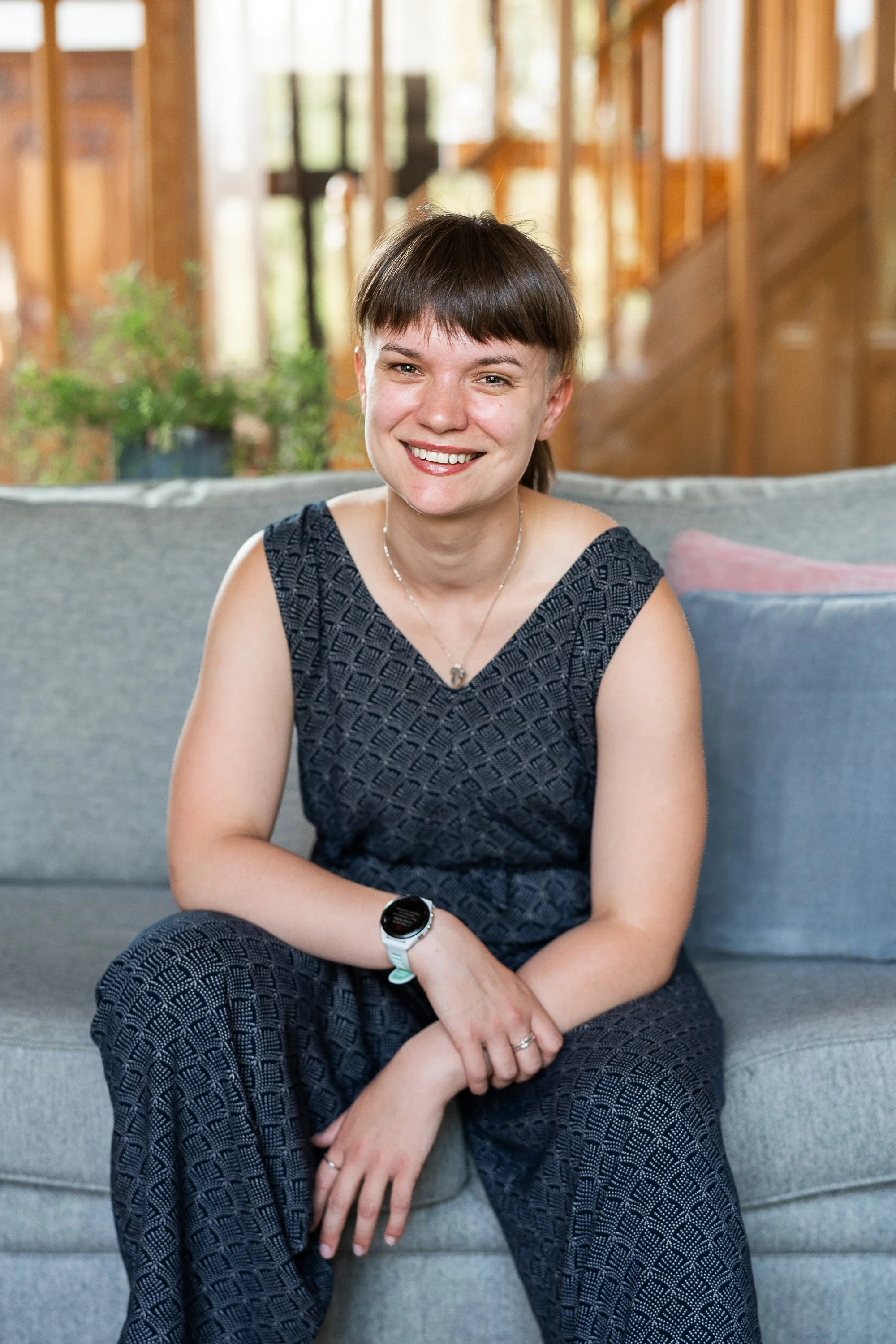 A therapist smiling and sitting on a gray sofa in a warmly lit room.