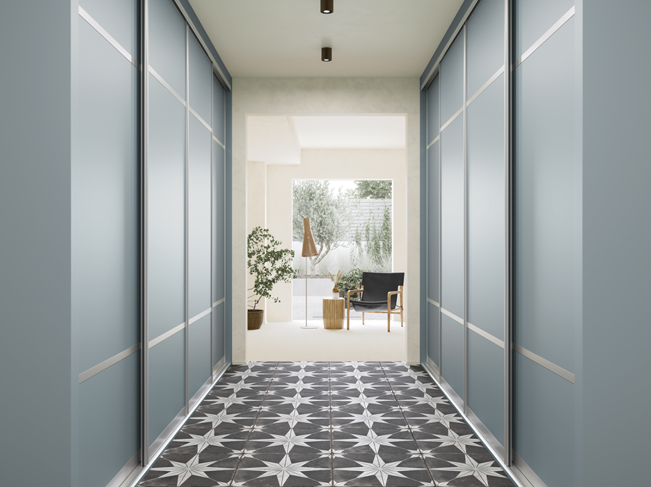 Hallway with blue sliding closet doors leading to a bright living space with black chair, potted plants, and patterned tile floor.