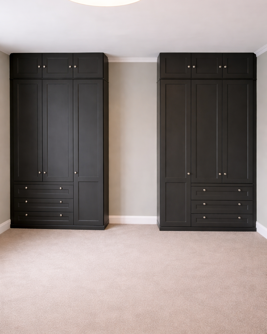 Two tall black cabinets with silver knobs in a room with beige carpet and light gray walls.
