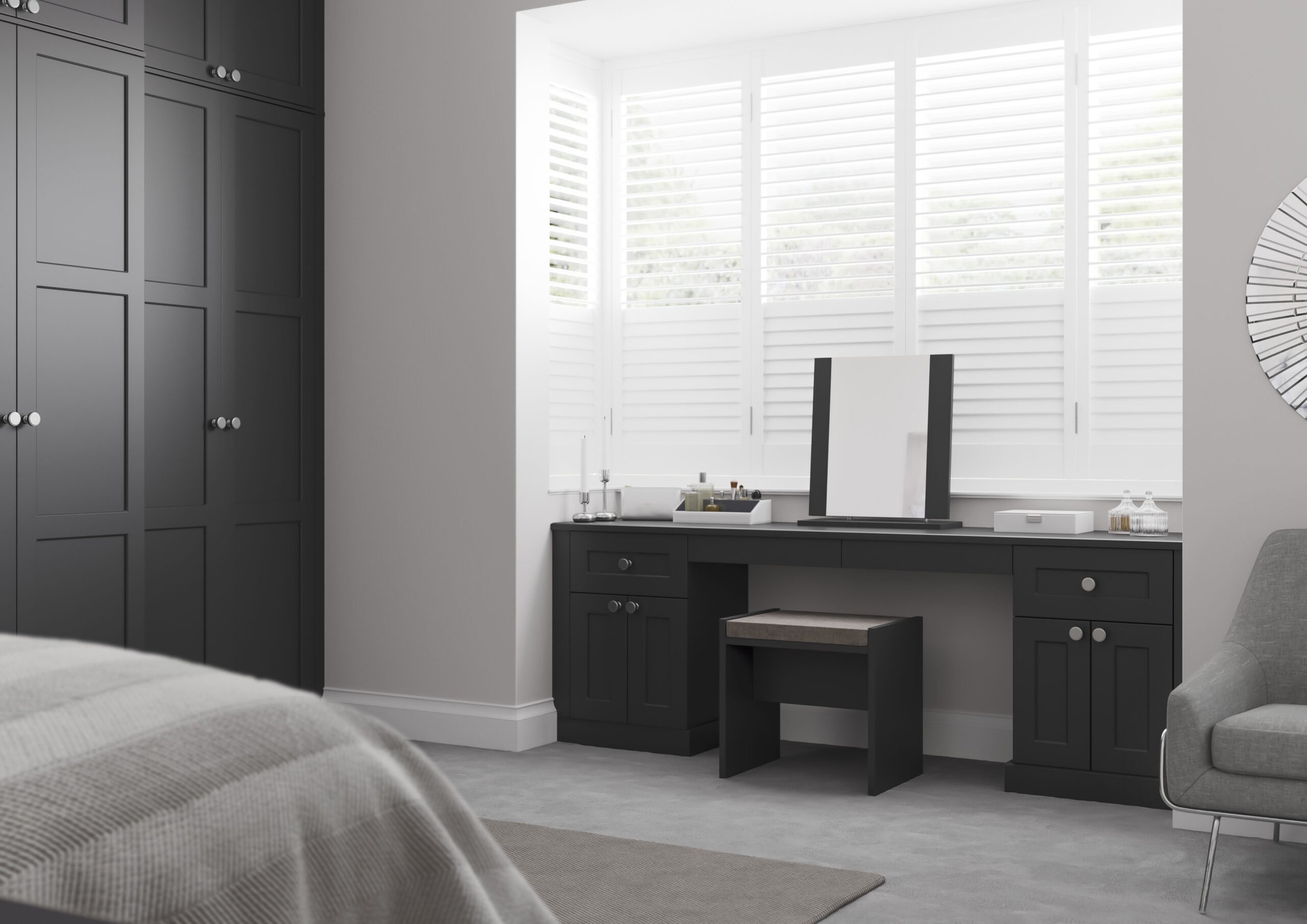 A modern bedroom with dark gray wardrobes, a black vanity table with a mirror, and a gray upholstered armchair. The room has large white plantation shutters on the window, letting in natural light. The bed has a textured beige blanket, and there is a