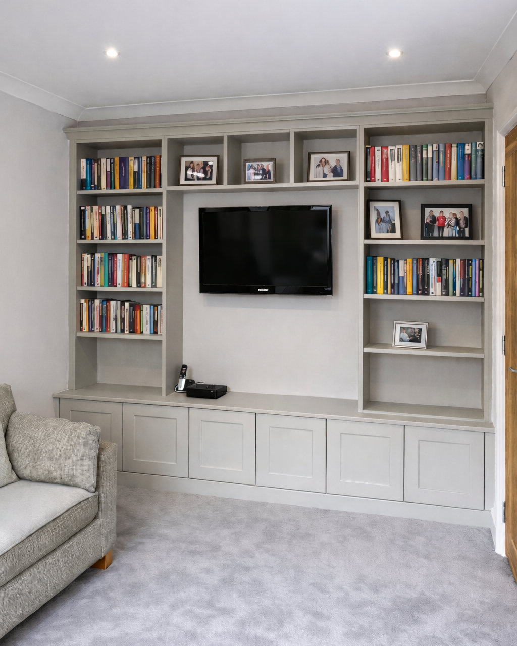 A built-in entertainment center with shelves filled with books and framed photographs, a flat-screen TV in the center, and a gray sofa on the left side.