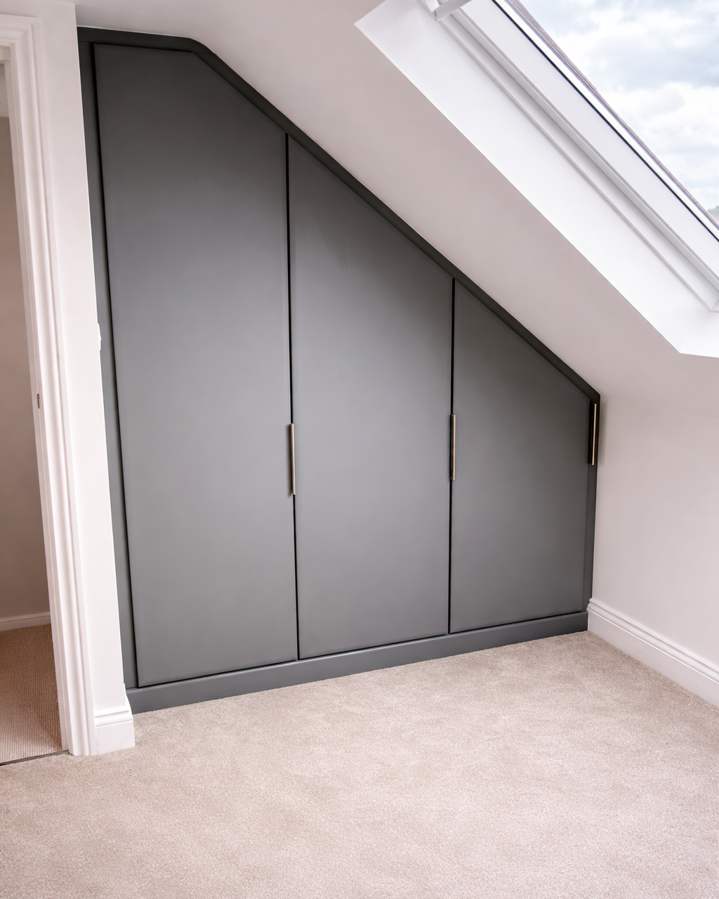 Gray built-in storage cabinets under a sloped ceiling with a skylight window.