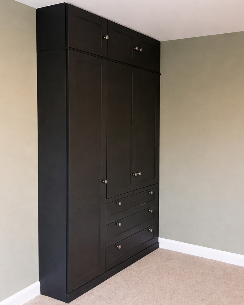 A large black wooden wardrobe with multiple doors and drawers in a room with beige carpet and light green walls.