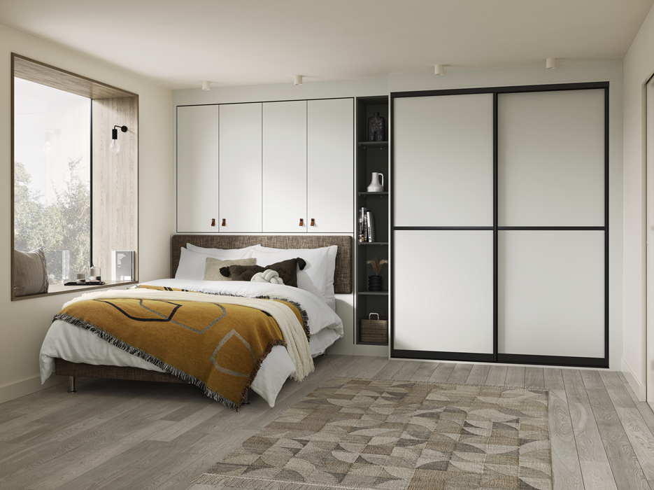Modern bedroom with a large bed, white bedding, accent pillows, a yellow blanket, a window seat with pillows, a built-in wardrobe with sliding doors, open shelves with decor items, a textured area rug, and natural light from a large window.