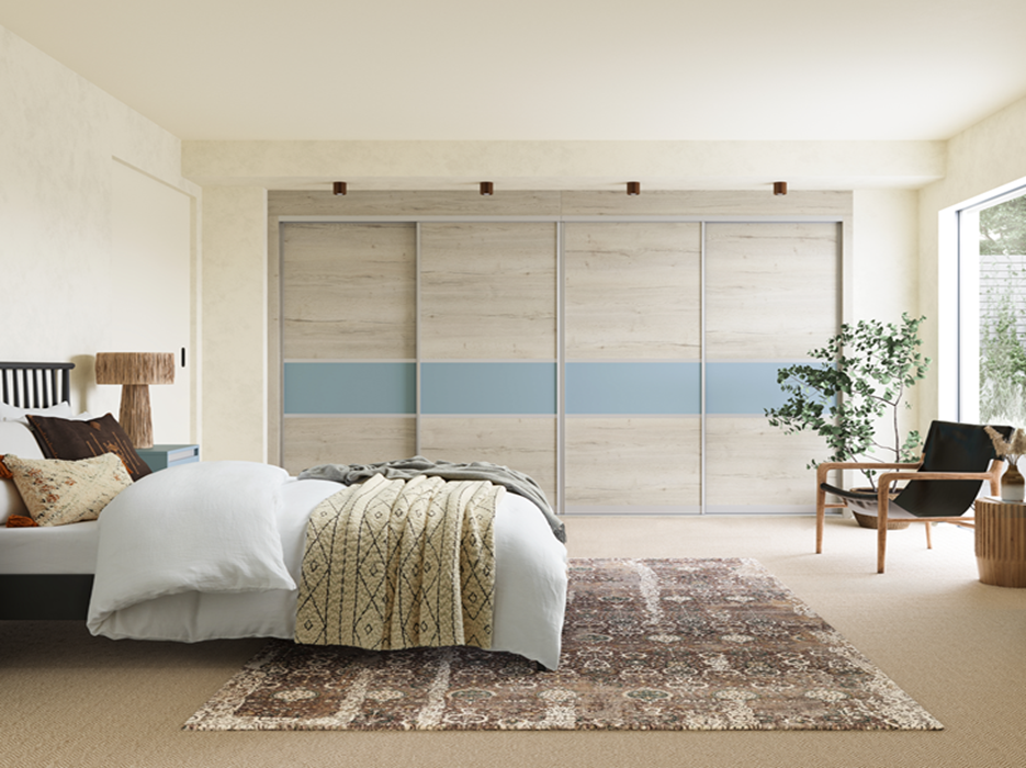 Bedroom with a large bed, patterned pillows, a throw blanket, a wooden chair with a cushion, a plant, a window, and sliding closet doors.