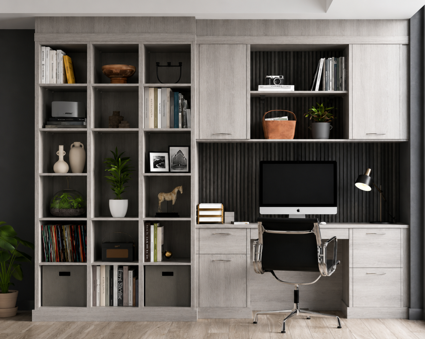 Modern home office with built-in light gray shelving and cabinets, black wall panel, desktop computer, black chair, desk lamp, and decorative items including vases, books, plants, framed photos, and art.