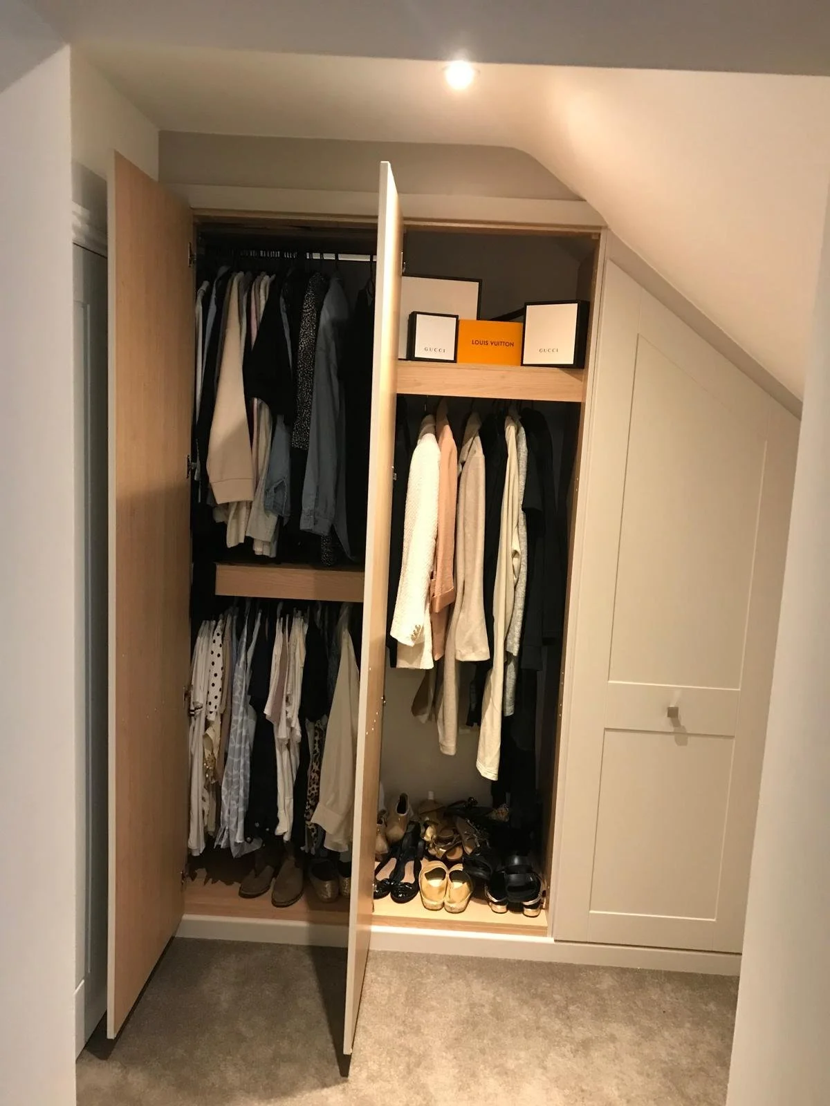 Open wardrobe with hanging clothes, shelves with boxes, and shoes at the bottom.