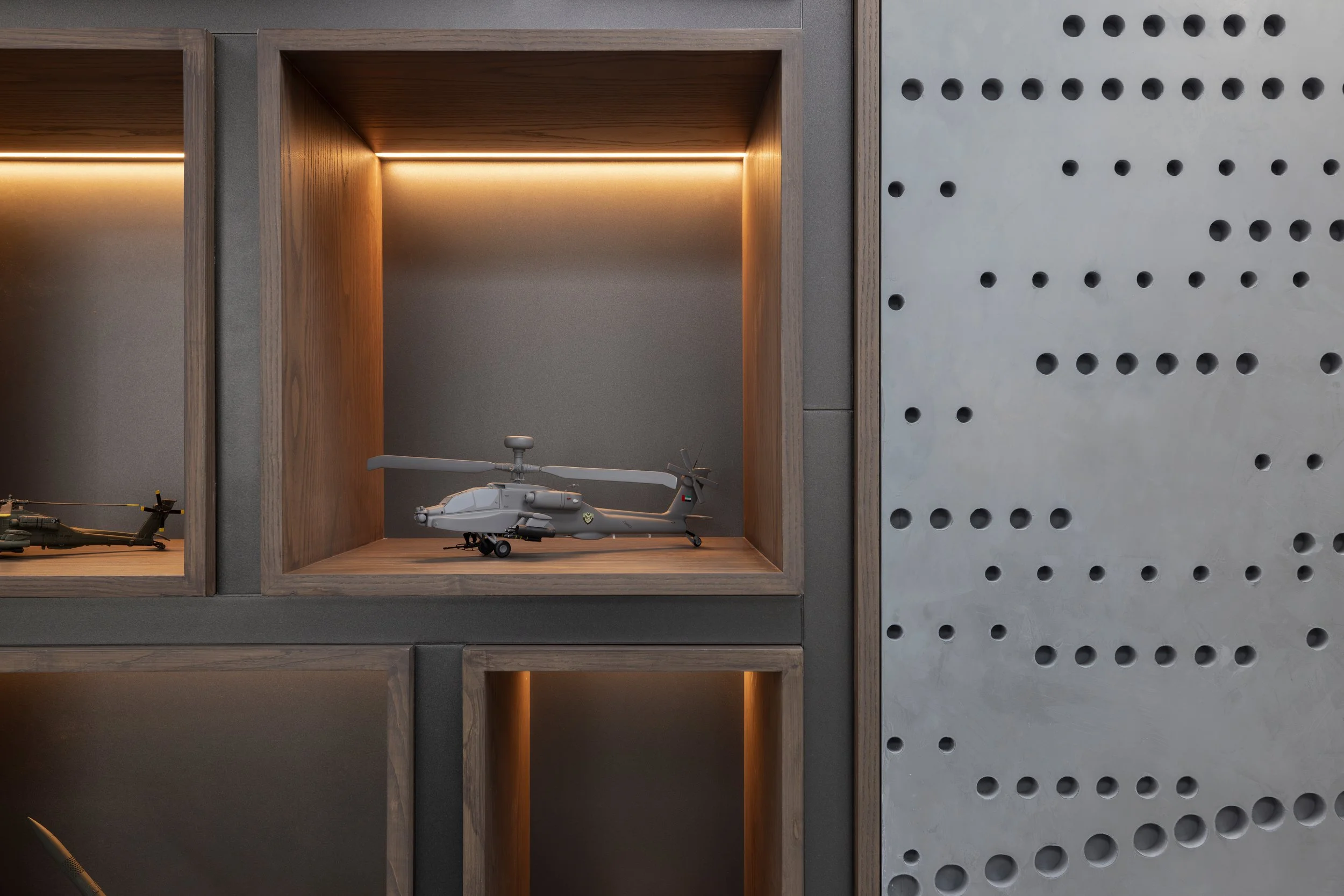 Display shelf with model helicopters inside wooden cubbyholes, set against a gray wall with a perforated pattern.
