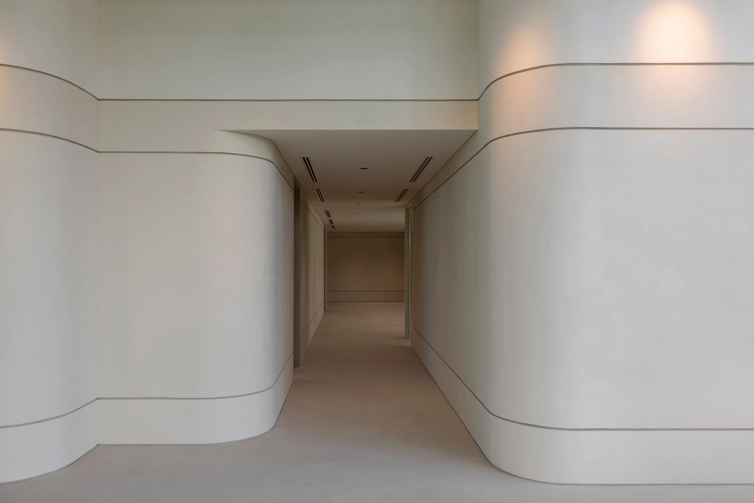 Minimalist corridor with white walls and curved lines, leading to a distant door or opening.