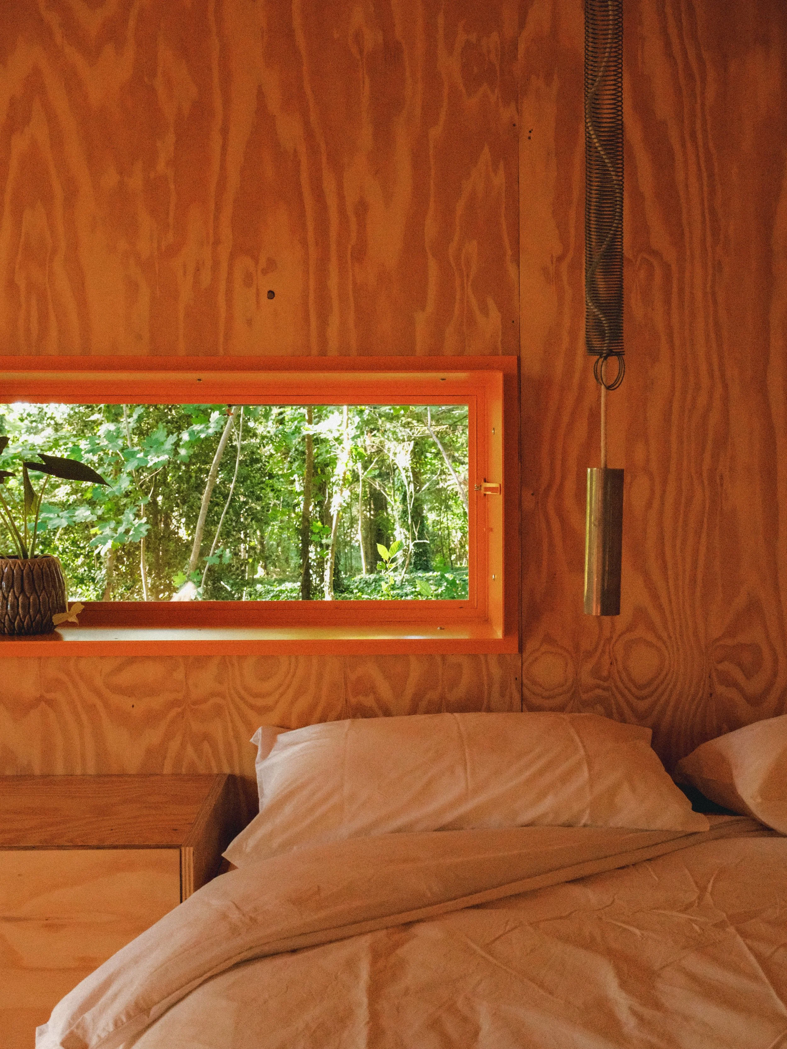 Un intérieur en bois avec un lit, deux oreillers et une fenêtre donnant sur une forêt verte.