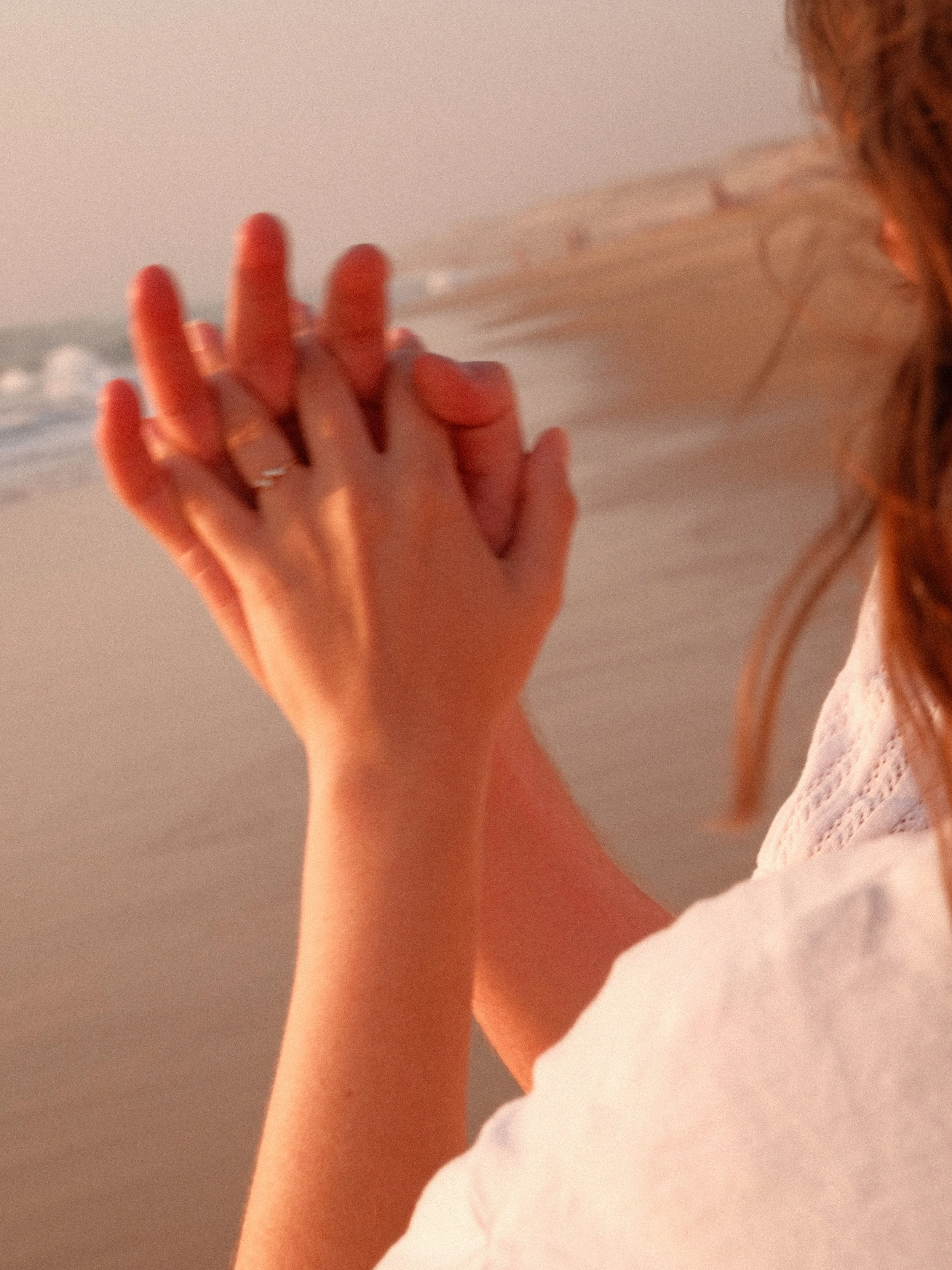Une main féminine portant une alliance, avec des vagues en arrière-plan lors d'un coucher de soleil, en bord de plage.