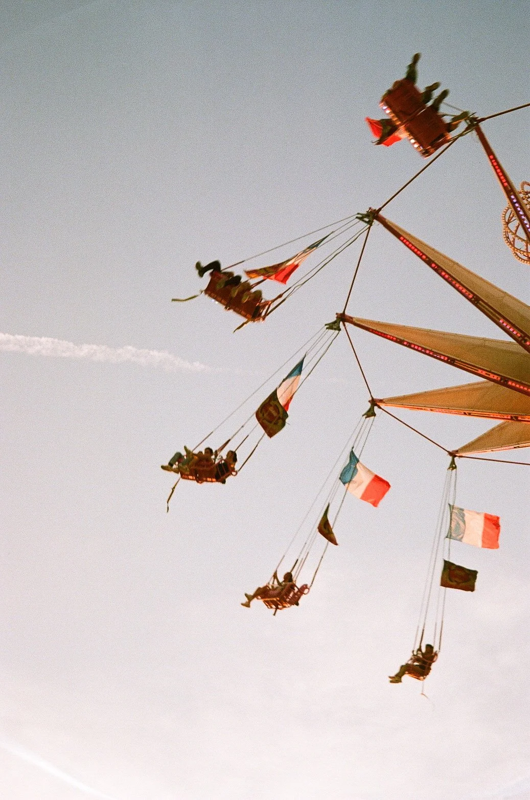 Chaise swing dans une fête foraine, décorée de drapeaux français, suspendue dans le ciel au coucher du soleil.
