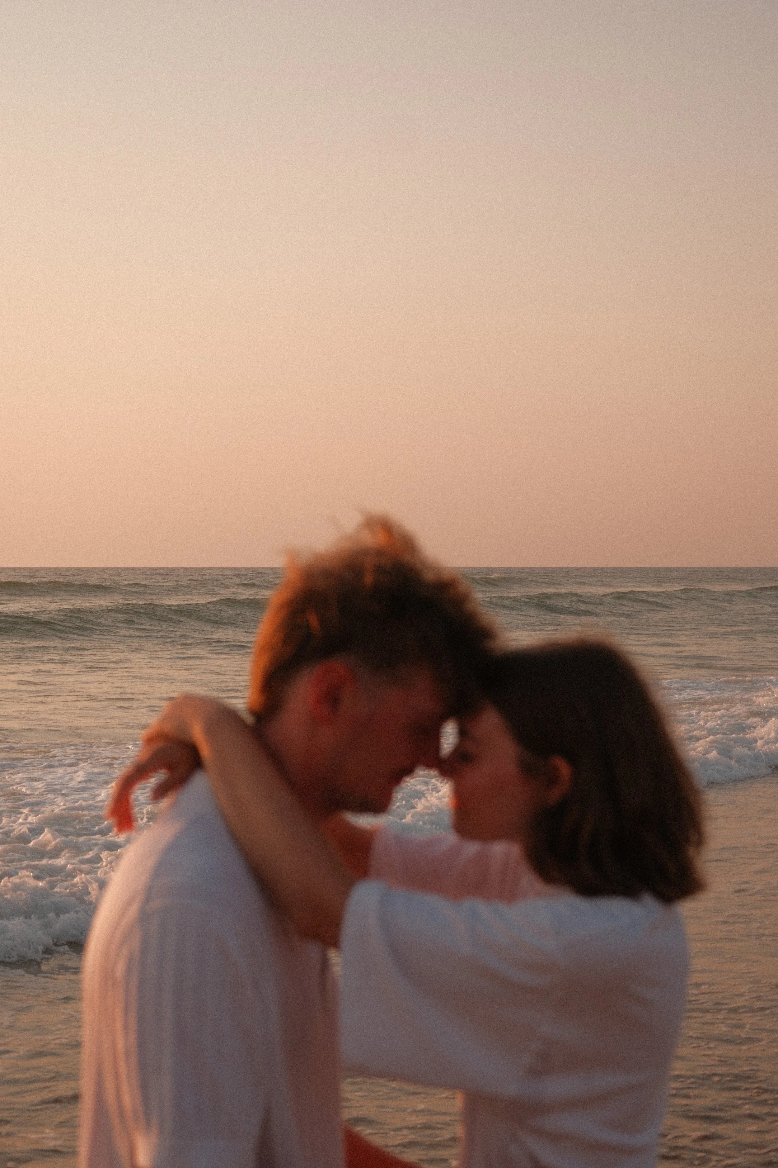 Deux personnes s'embrassent sur la plage au coucher du soleil, avec la mer en arrière-plan.