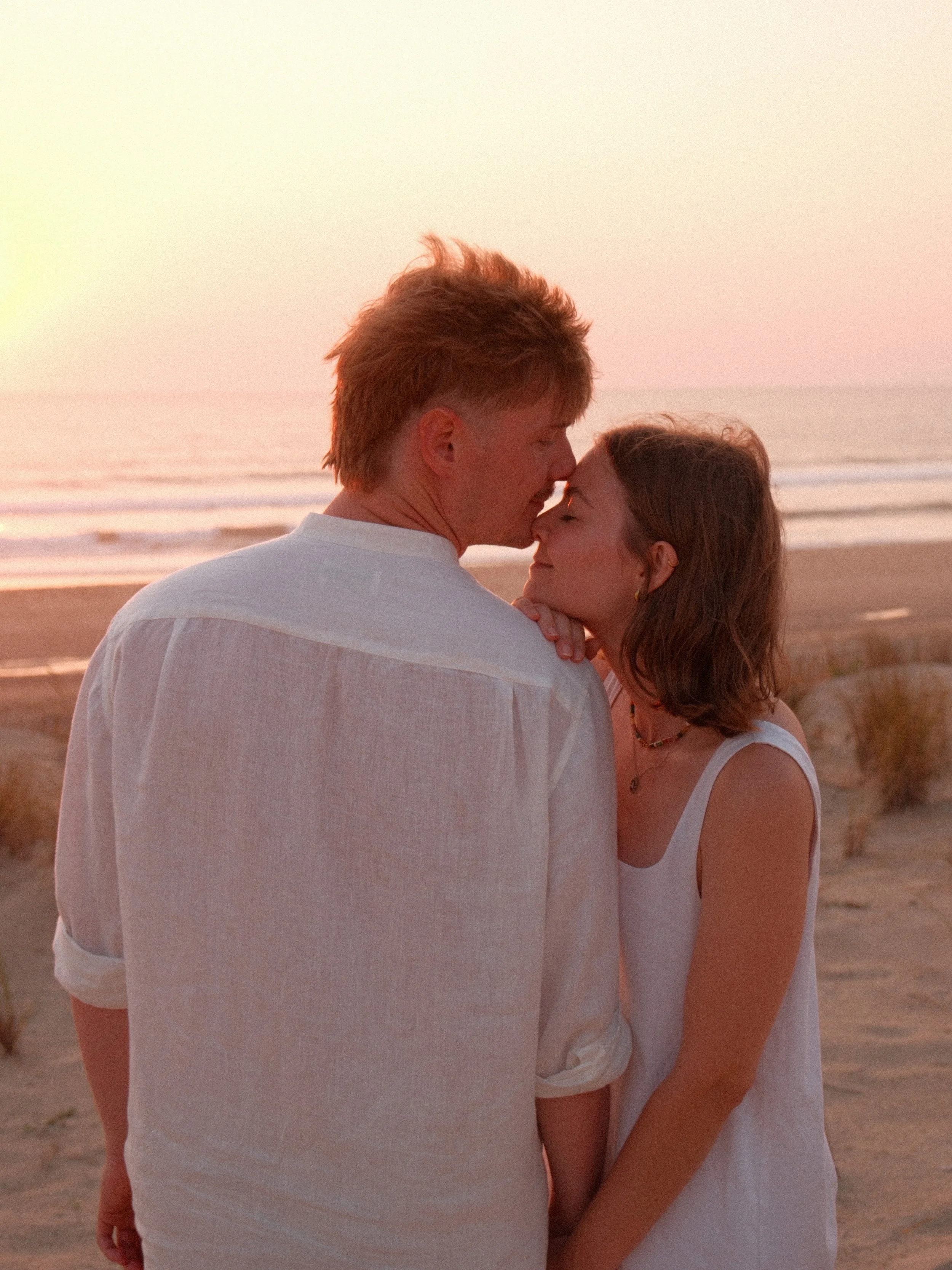 Un couple qui s'embrasse sur la plage au coucher du soleil, vue de dos, avec la mer en arrière-plan.