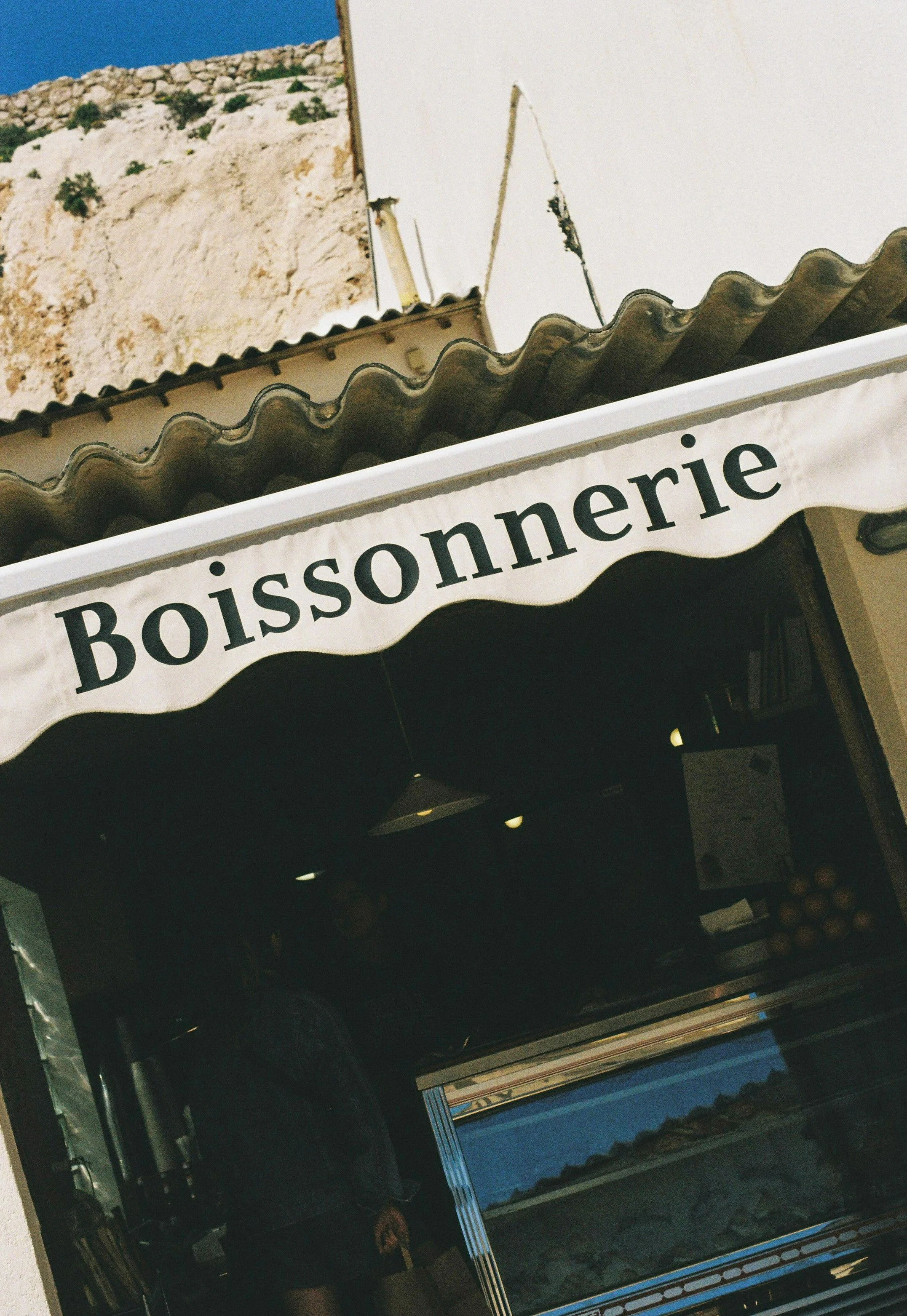 Un stand de boisson avec une enseigne portant l'inscription 'Boissonnerie' en français, situé à côté d'un bâtiment en pierre remarquable.
