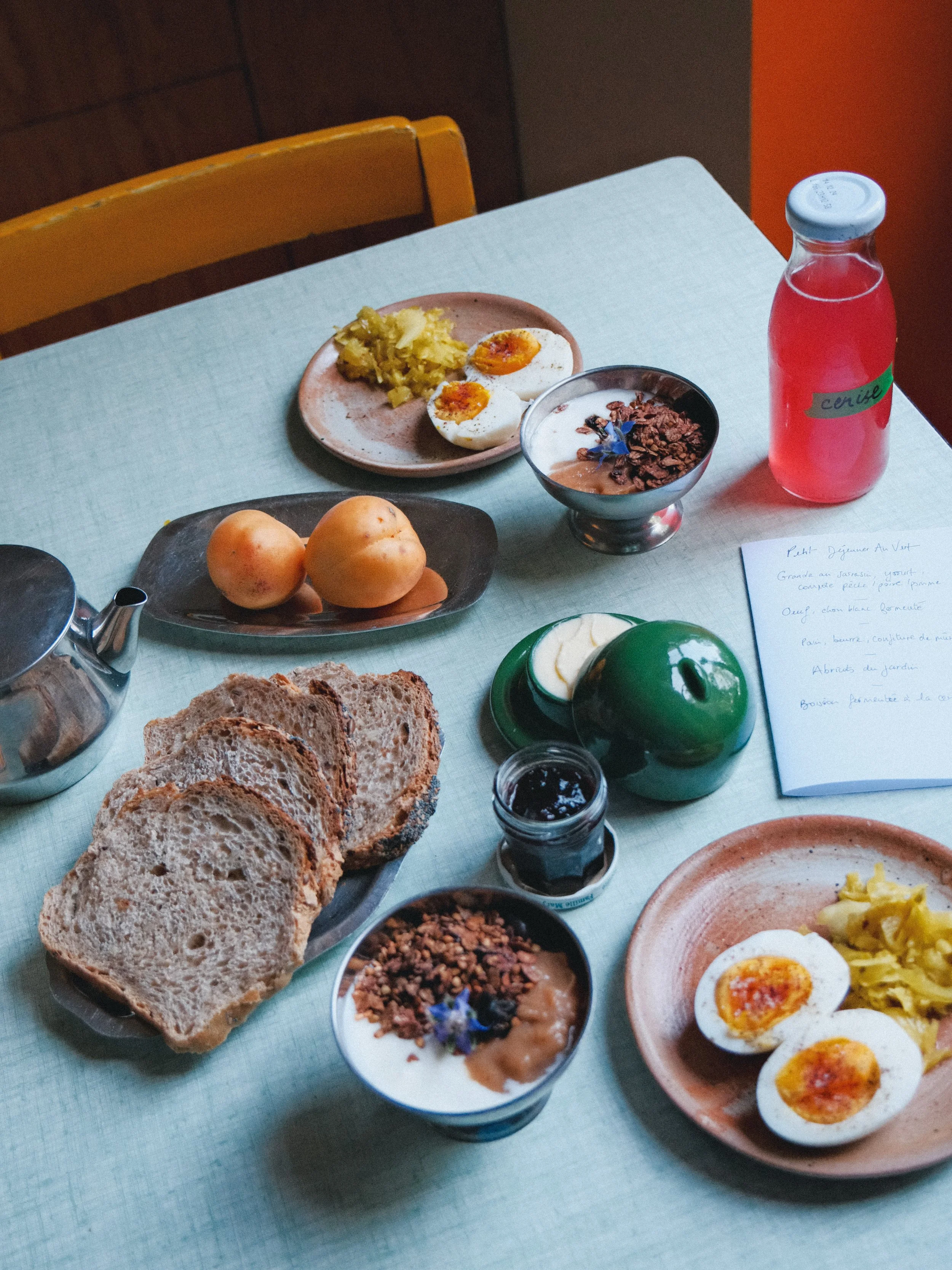 Petit déjeuner avec œufs mollets, pain complet, yaourt, confiture, fruit et boisson à la cerise.