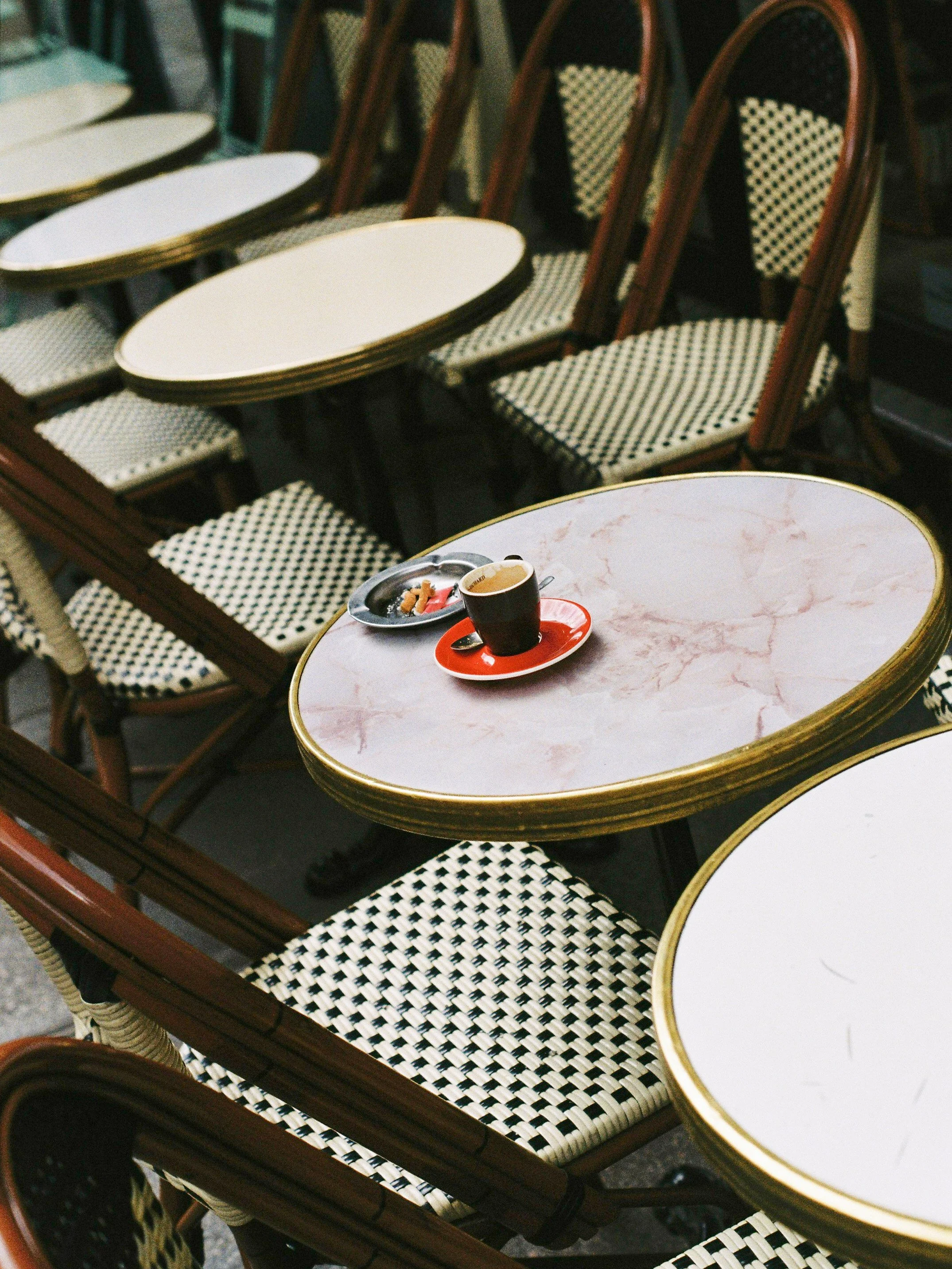 Chaises en bois avec assises et dossiers tissés en motif vichy noir et blanc, entourant des tables rondes avec surfaces en marbre blanc veiné.