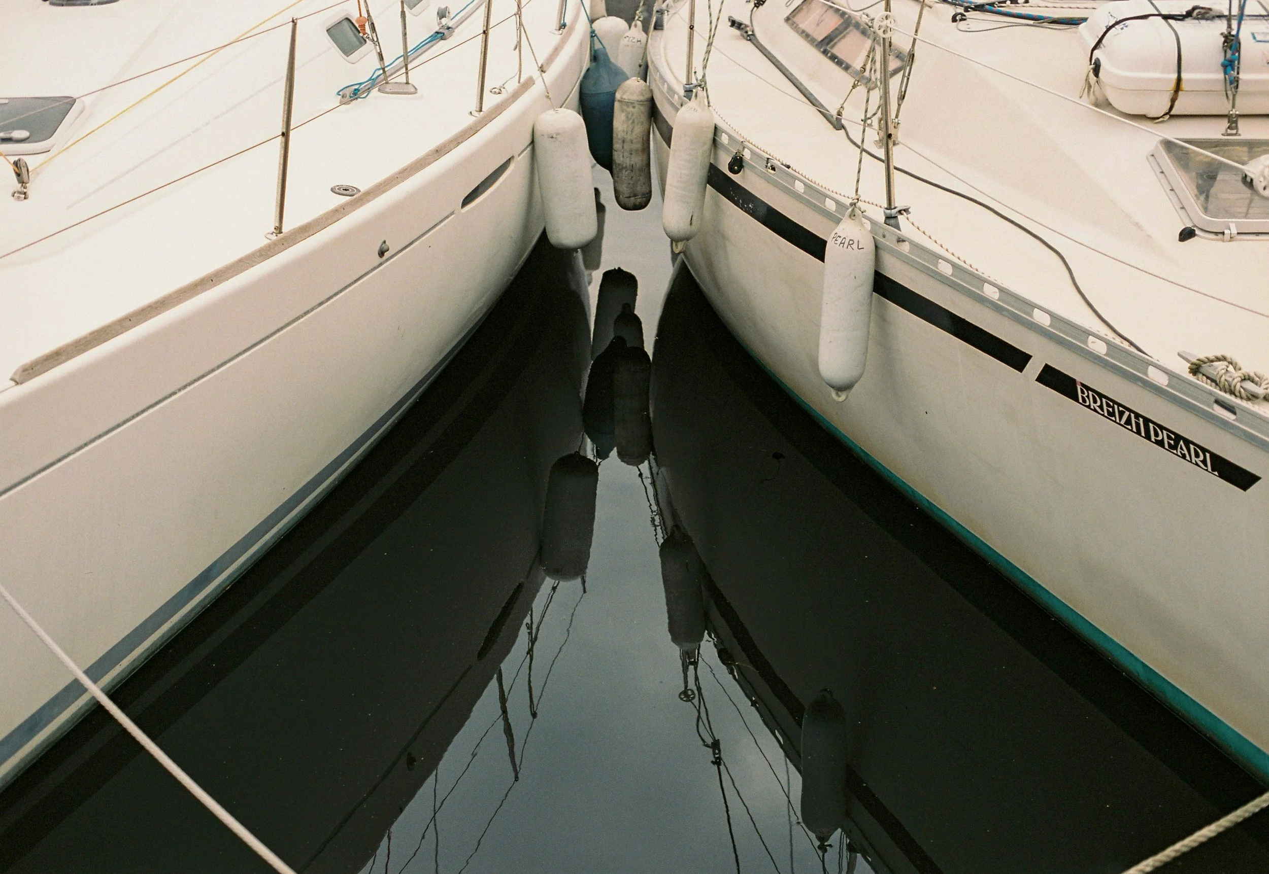 Deux bateaux de plaisance amarrés côte à côte avec des ballasts flottant dans l'eau, vue depuis le quai.