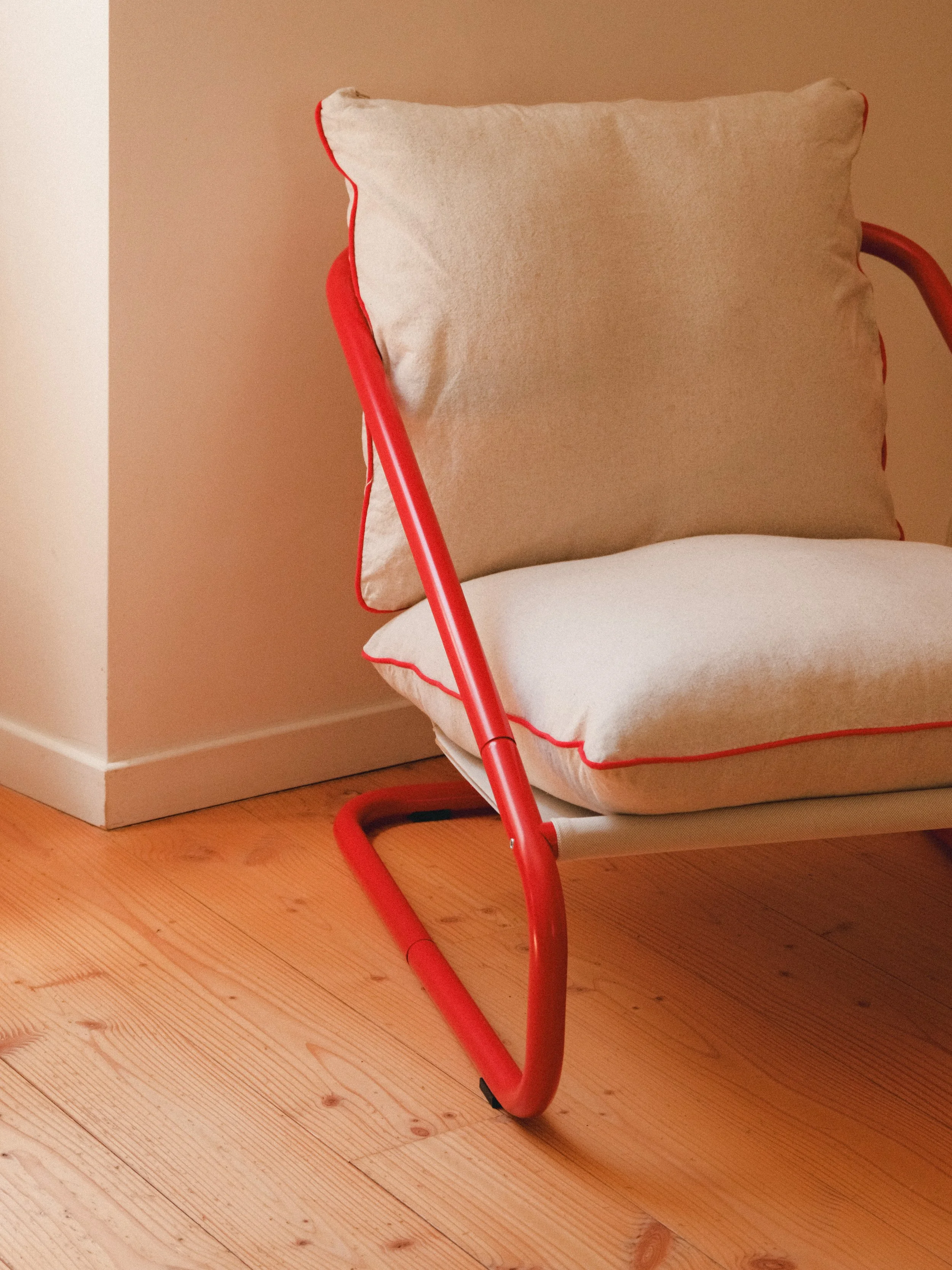 Chaise en métal rouge avec un coussin beige, placée dans une pièce au mur beige et au sol en bois.