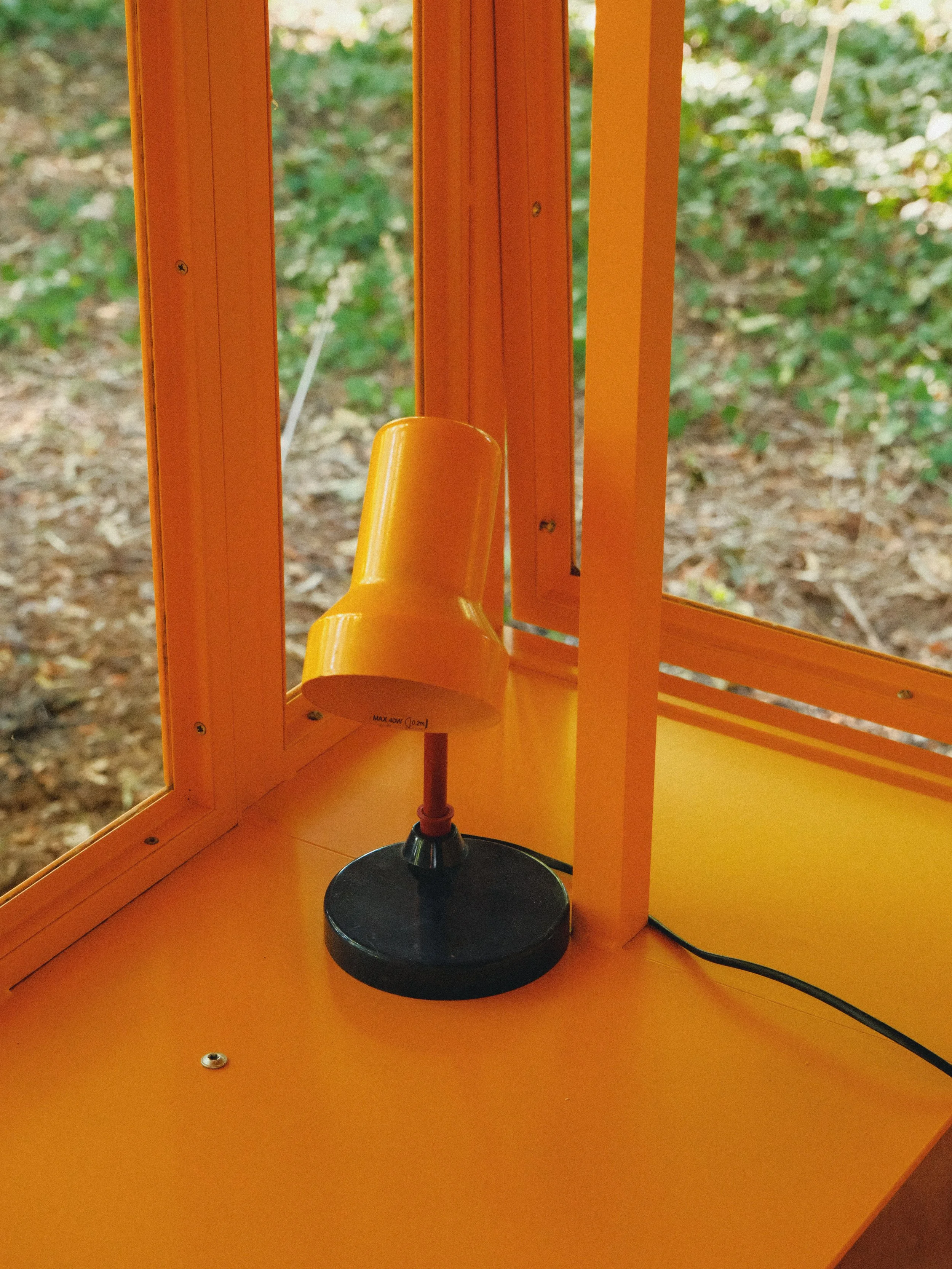 Étude de laboratoire avec une lampe de bureau, orange, au centre, sur une surface orange, avec un panneau orange en arrière-plan et un fond de forêt.
