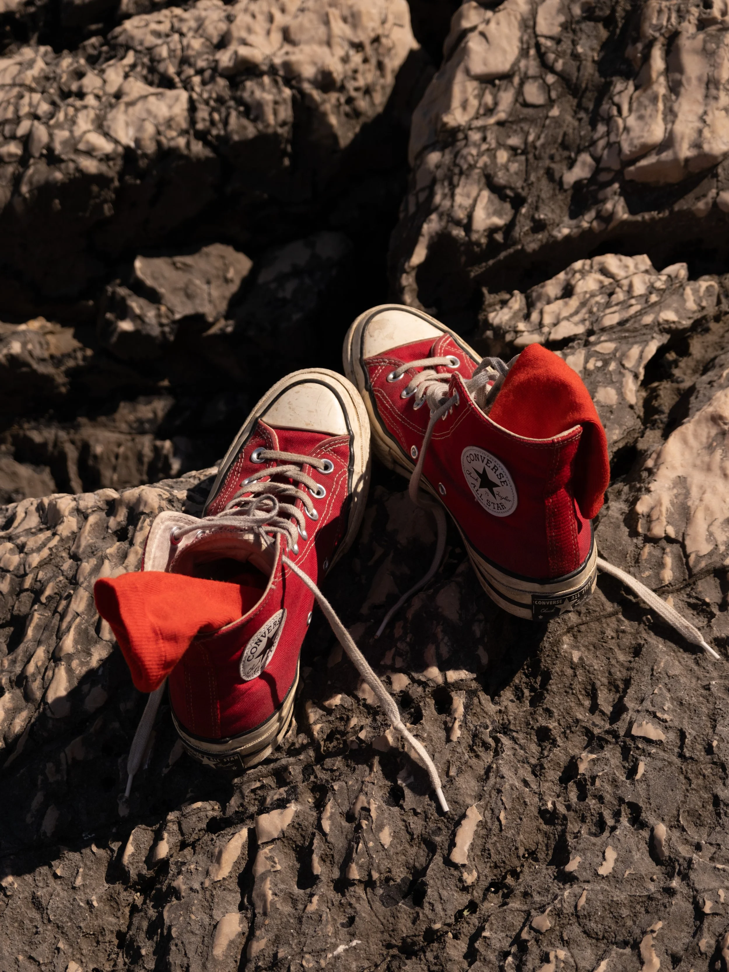 Chaussures Converse rouges posées sur des rochers, avec un lac ou une rivière en arrière-plan.