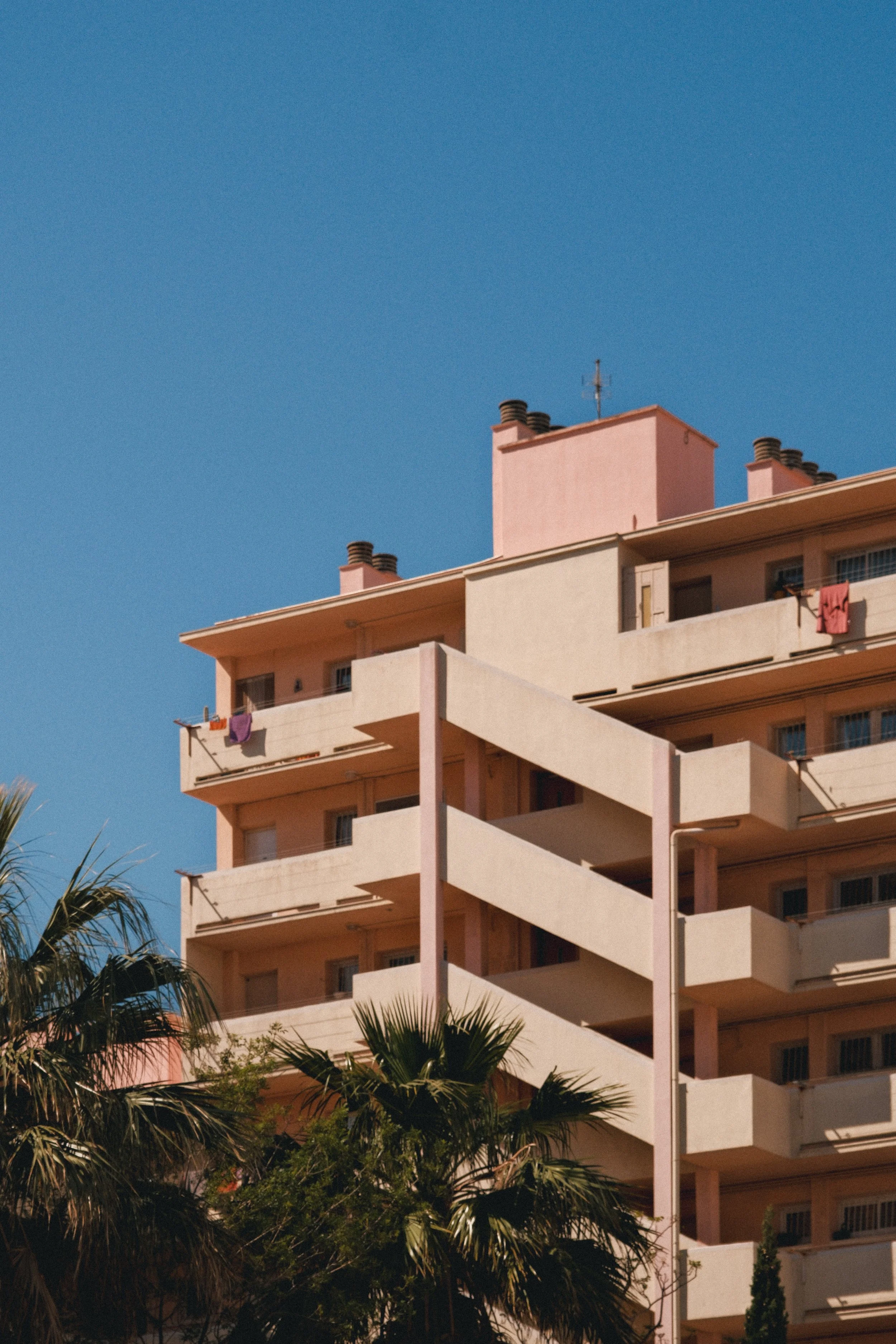 Un immeuble résidentiel avec plusieurs balcons, des cheminées, et des vêtements suspendus à l'extérieur, sous un ciel bleu clair.
