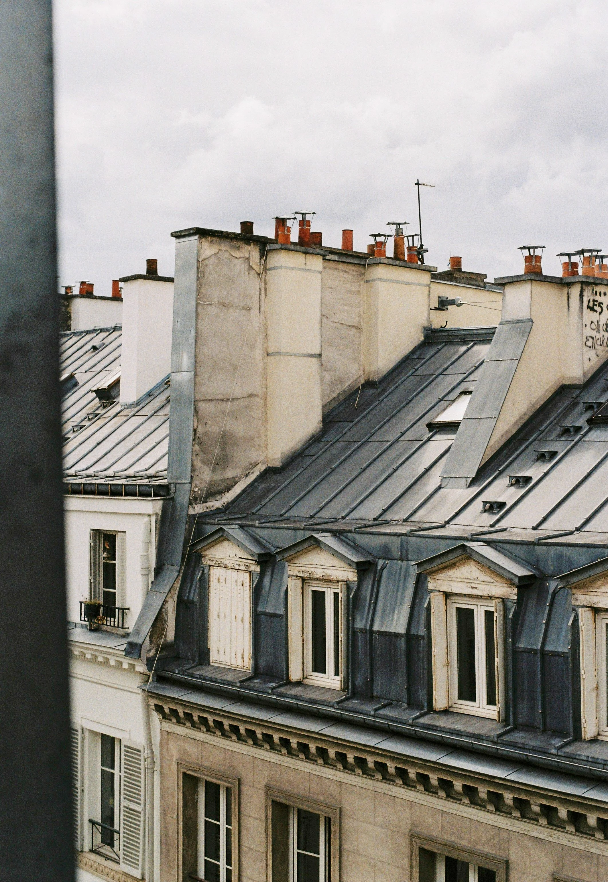 Vue des toits d'immeubles parisiens avec des cheminées en brique et des fenêtres.
