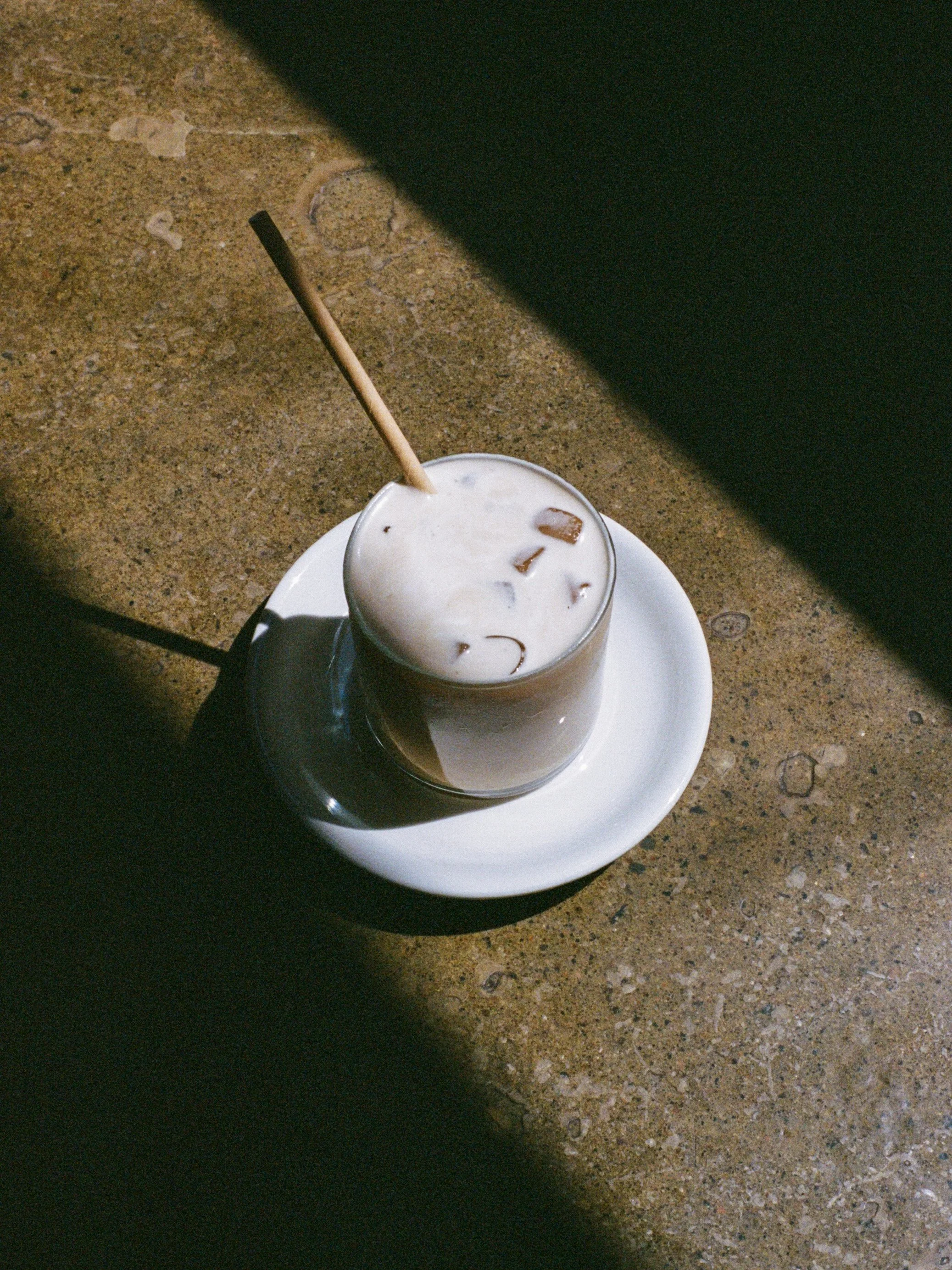 Verre de café glacé avec glaçons, servi sur une assiette blanche sur une surface en pierre.