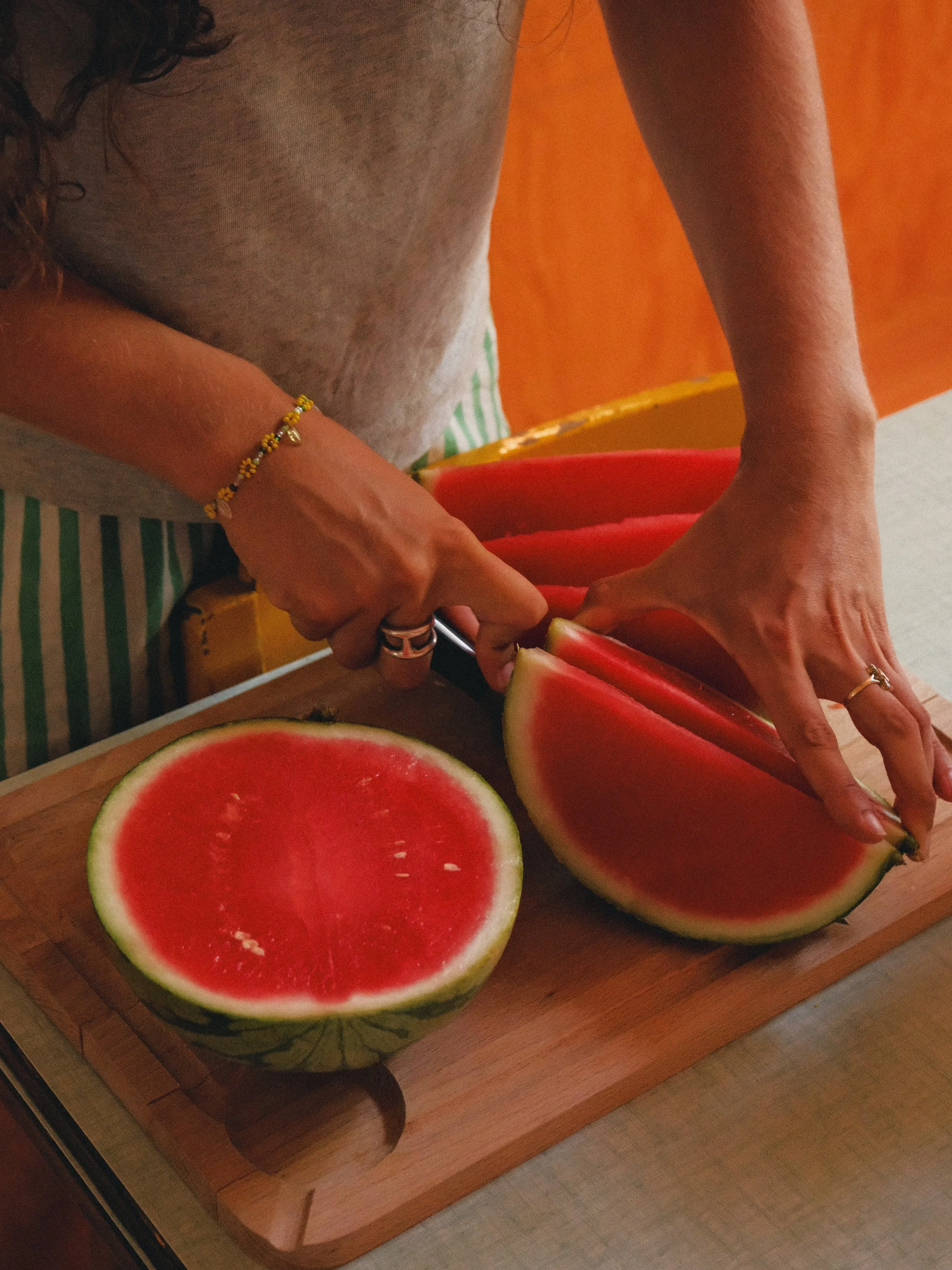 Personnes coupant un melon d'eau rouge avec un couteau sur une planche en bois.