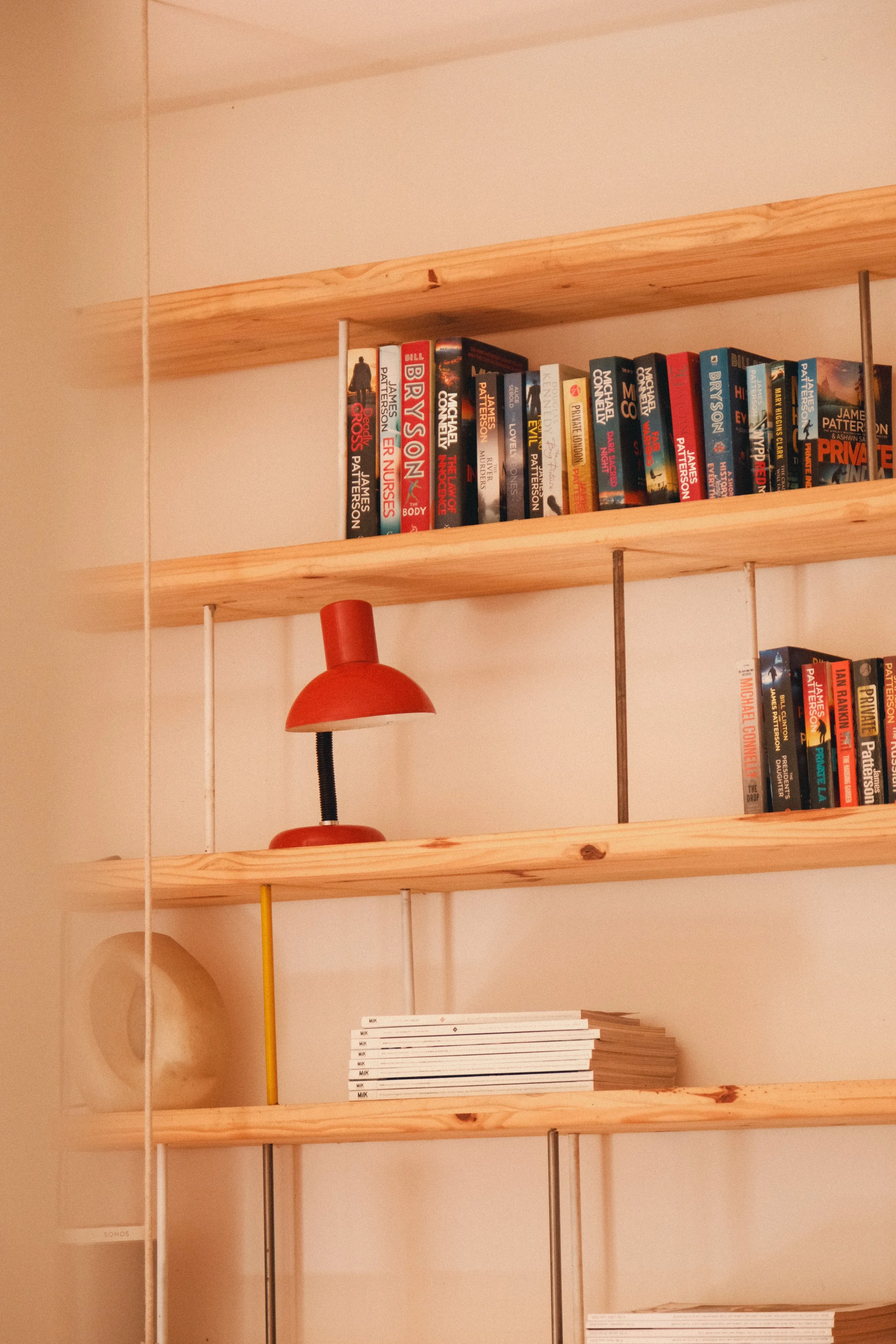 Étagères en bois avec des livres et une lampe rouge, avec des piles de livres en dessous.