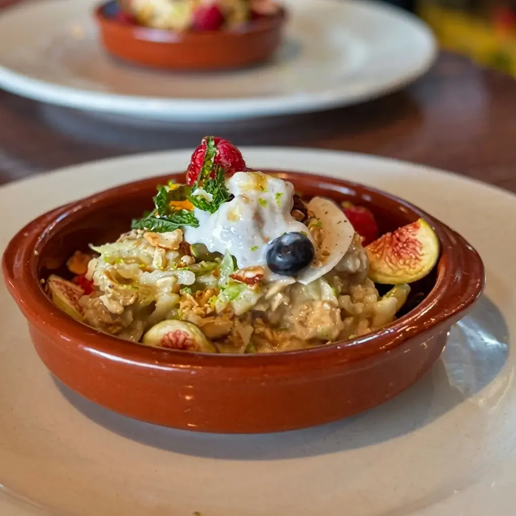 A bowl of oatmeal topped with strawberries, blueberries, figs, whipped cream, and chopped nuts, served on a white plate.