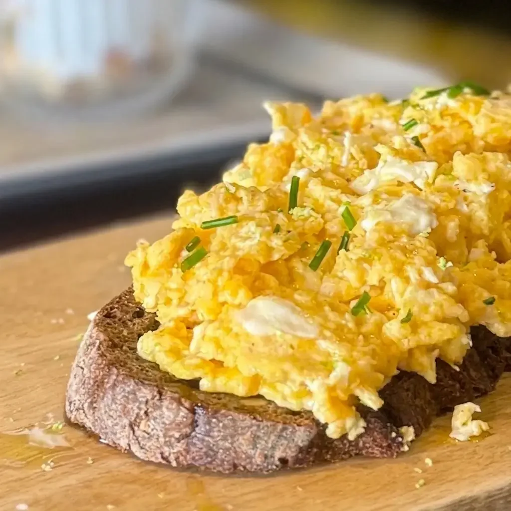 Scrambled eggs with green chives on a slice of toasted bread.