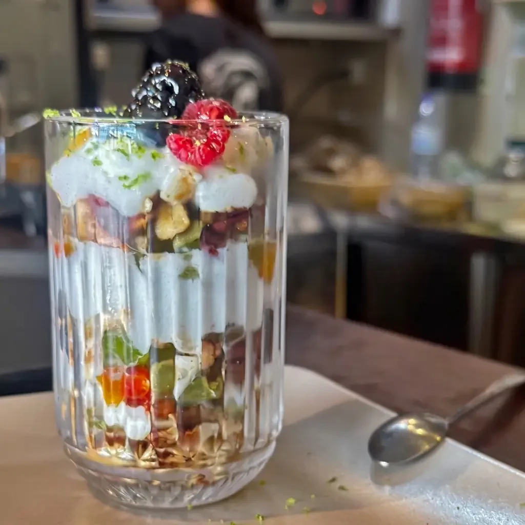A layered dessert in a clear glass with fruit, whipped cream, and toppings, garnished with blackberries and raspberries.