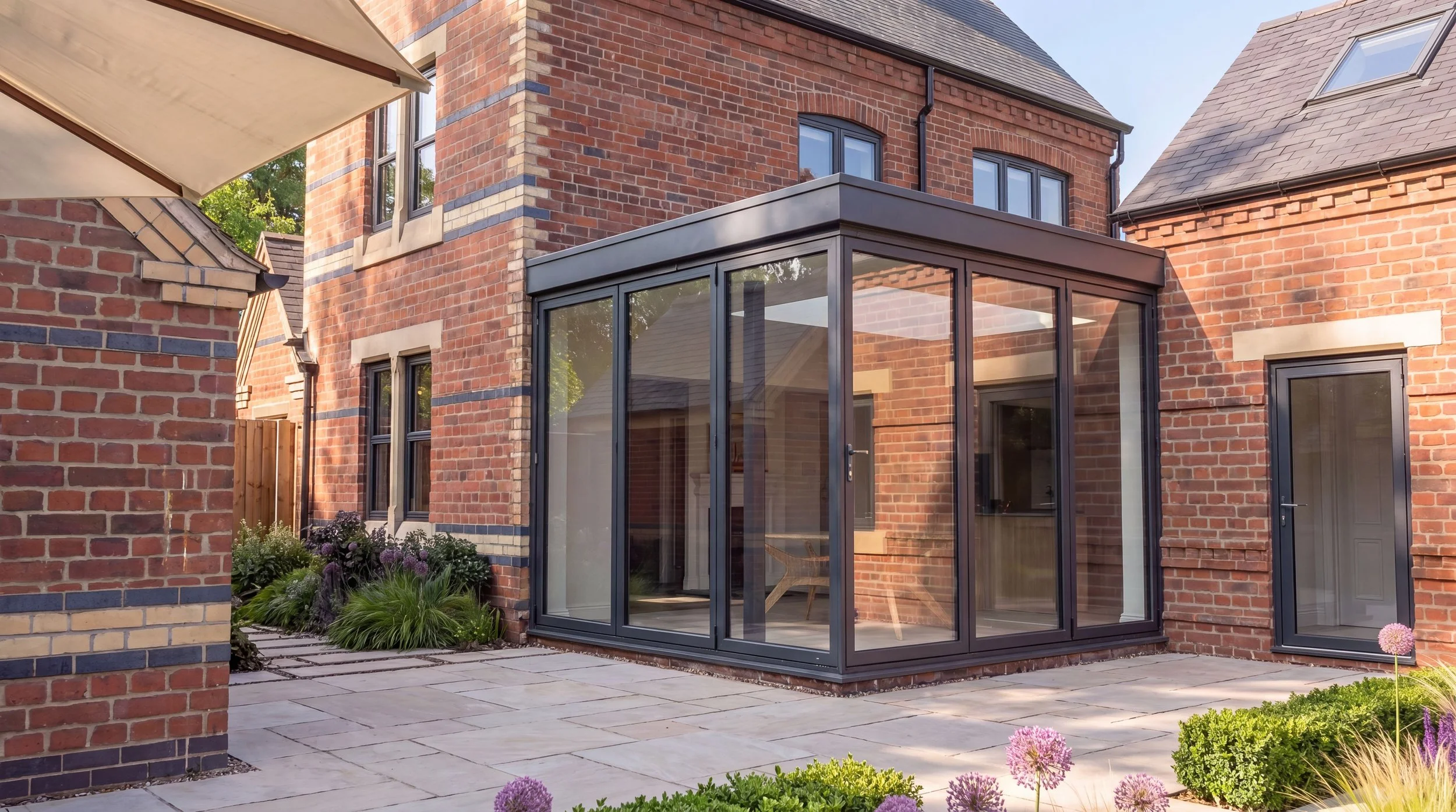 Brick house with glass sunroom, garden with purple flowers, and paved patio