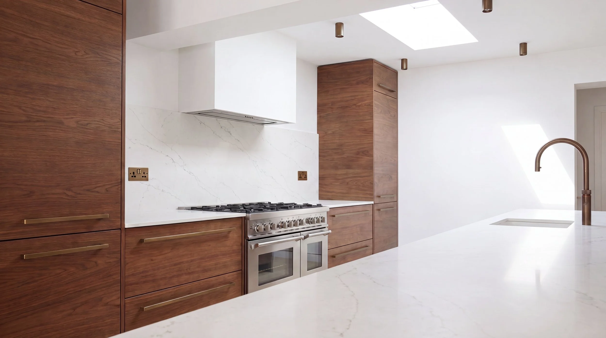 Modern kitchen with wooden cabinets, white marble countertops, and a sleek bronze faucet. Skylight overhead provides natural light.