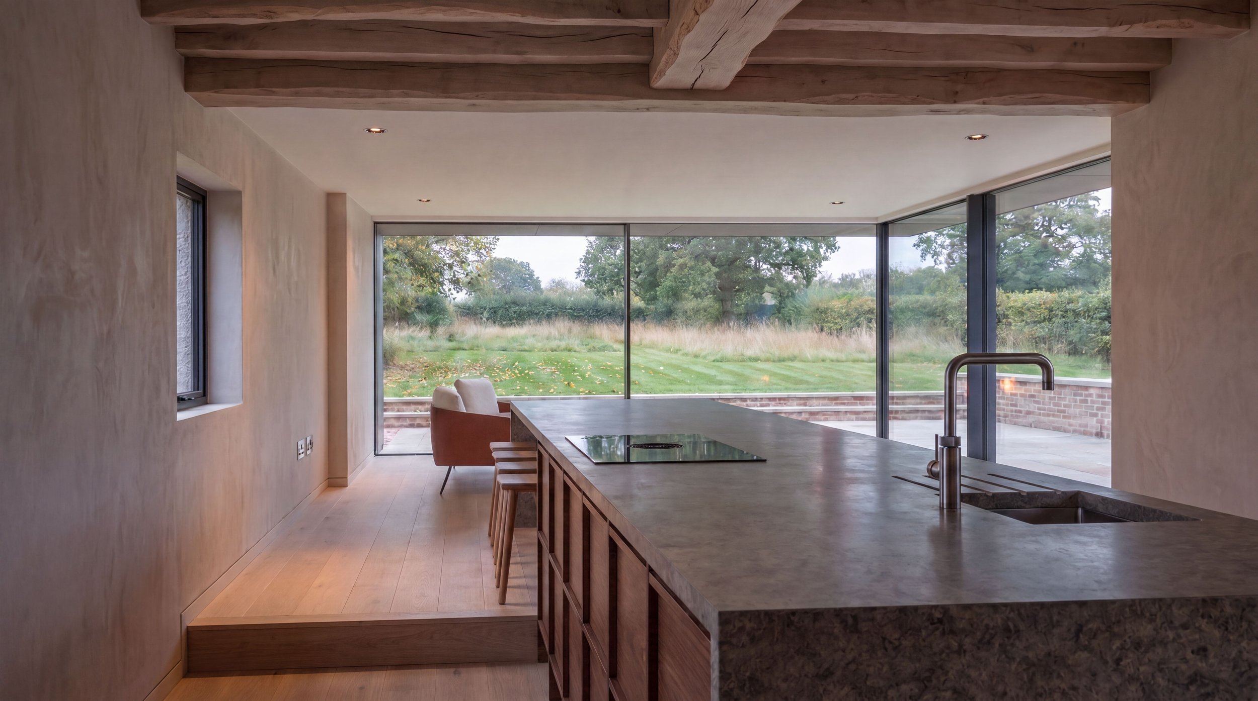 Modern kitchen with a large window overlooking a grassy backyard with trees, a beige wall, and a wooden countertop with a sink and a faucet.