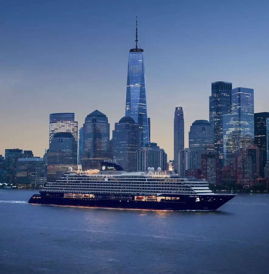Nighttime city skyline with tall skyscrapers and a large cruise ship on the water in the foreground.