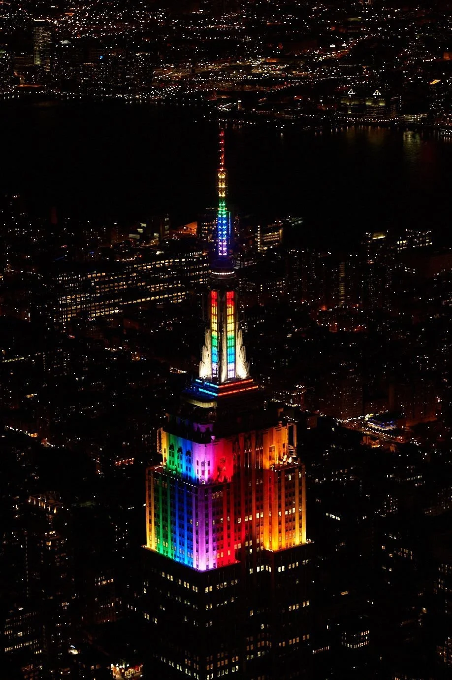 Night view of the Empire State Building illuminated with rainbow colors, reflecting pride and diversity, in New York City skyline.